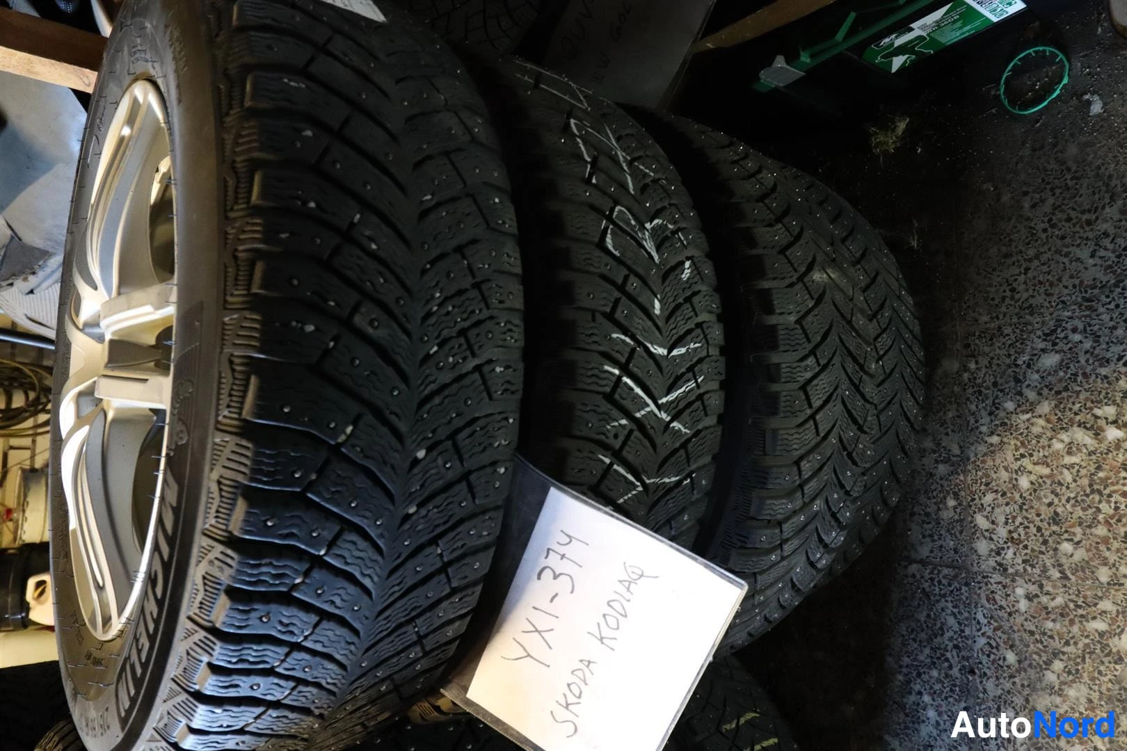 Yksityiskohta: Pinossa talvirenkaita niiteillä ja alumiinivanteilla; lapuissa käsinkirjoitettu teksti 'YX1-3714 SKODA KODIAQ' ja 'KULUKORVAUS'