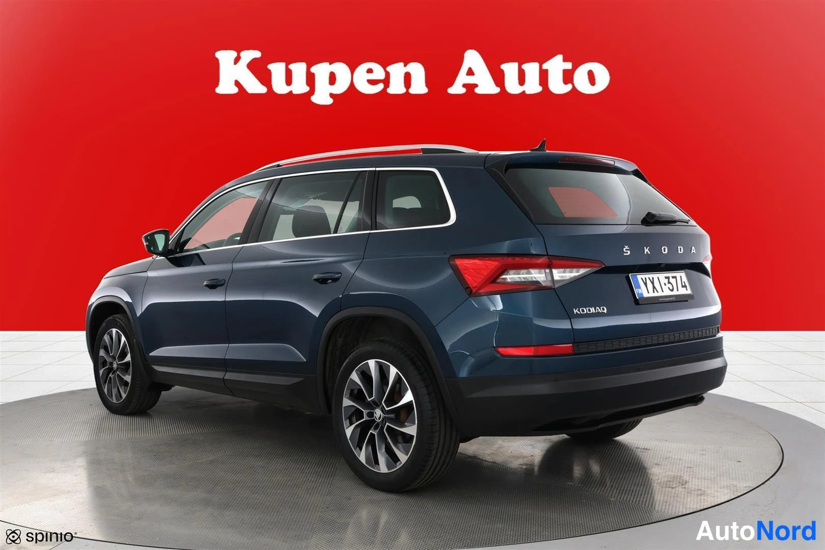 Takaviisto: Sininen Skoda Kodiaq taka‑kolmannesvasemmalta kuvattuna, Kodiaq‑teksti takaluukussa, punainen tausta.