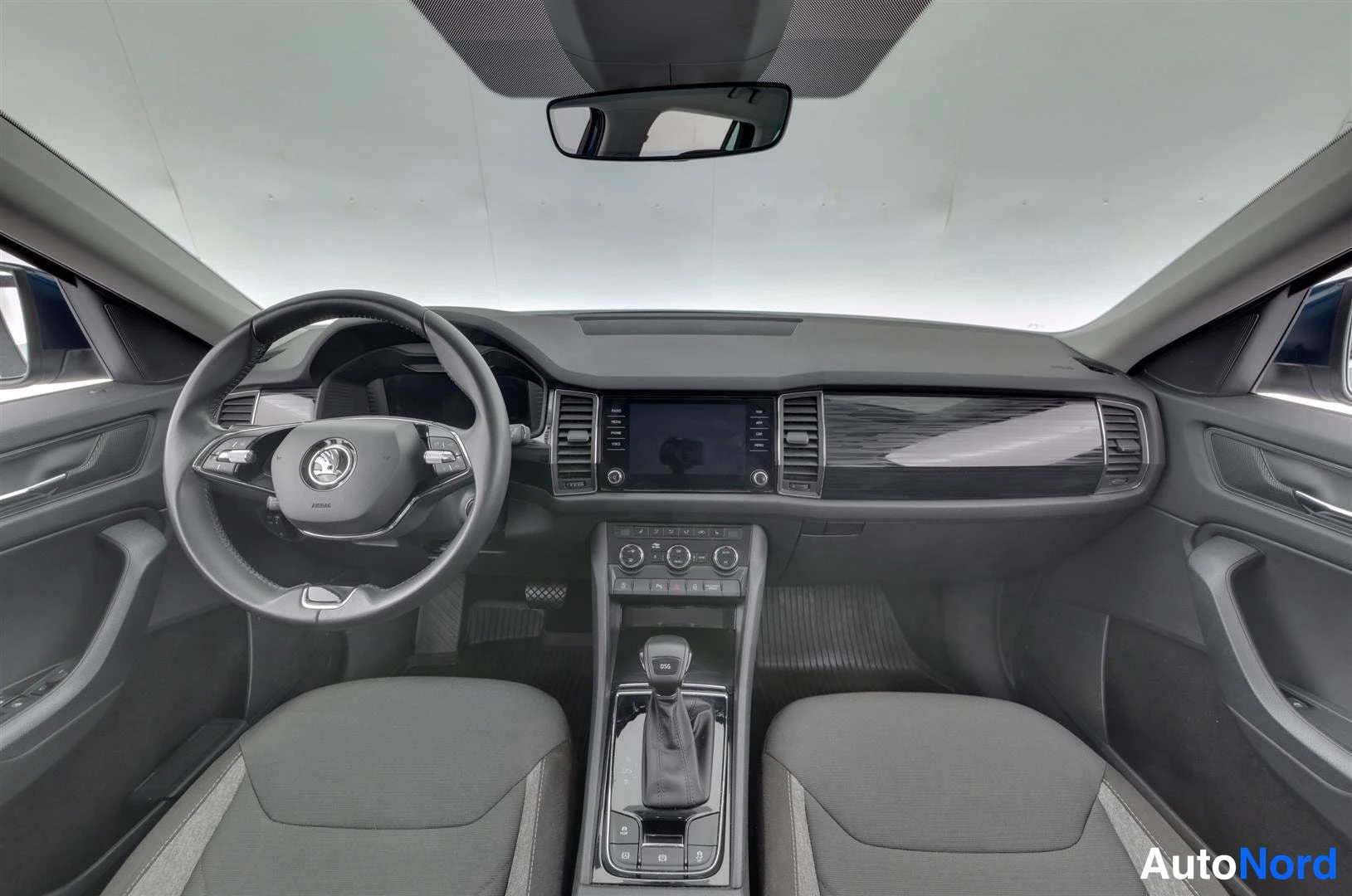 Muu: Skoda Kodiaqin ohjaamo suoraan edestä: ohjauspyörä, keskikonsolen infotainmentnäyttö, automaattivaihteiston valitsin ja kaksi etuistuinta.