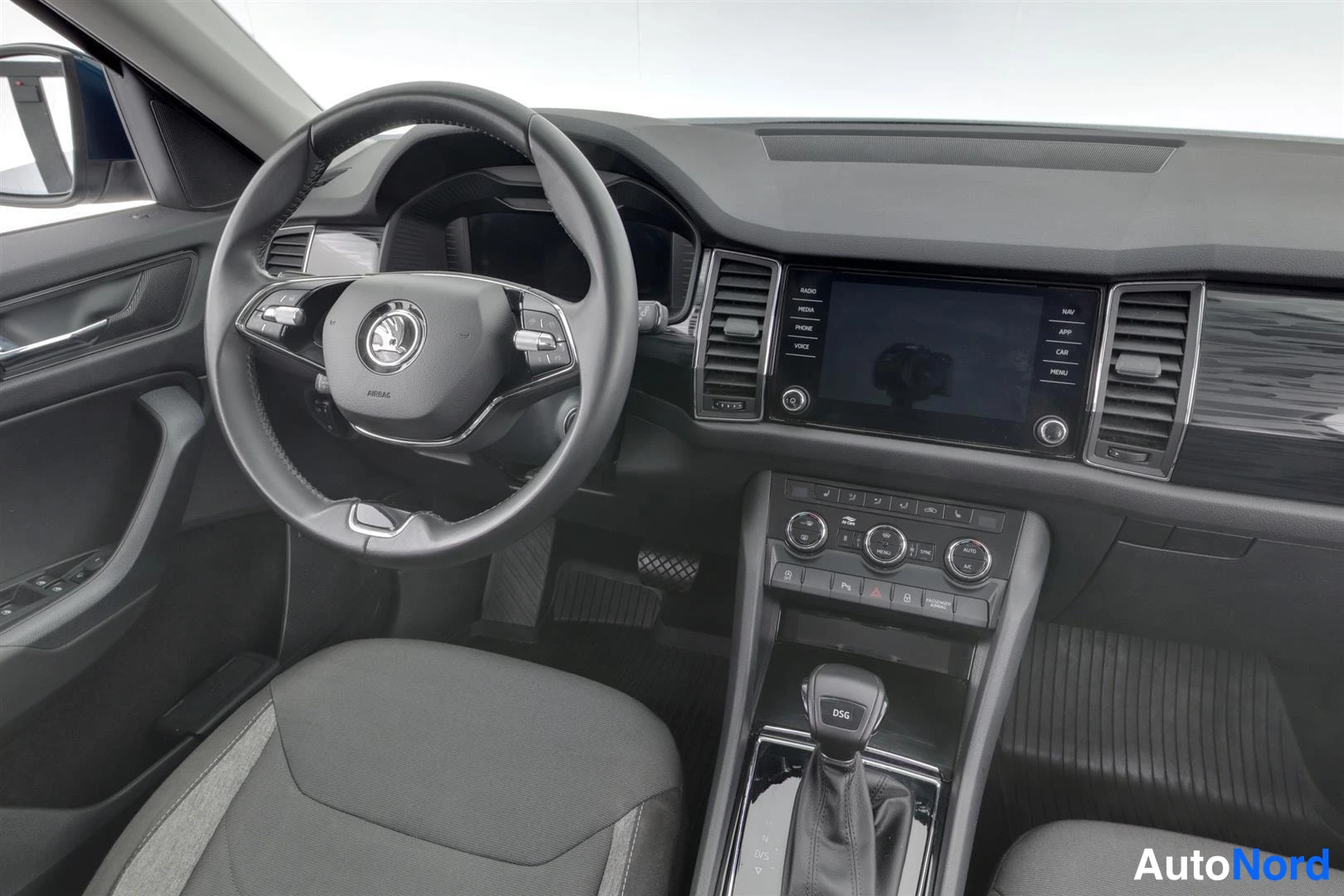 Muu: Skoda Kodiaqin kuljettajan puolen ohjaamo: ohjauspyörä, radiovälilehdet (RADIO, MEDIA, PHONE, VOICE, NAV, APP, CAR, MENU), ilmastointisäätimet ja DSG-vaihteenva