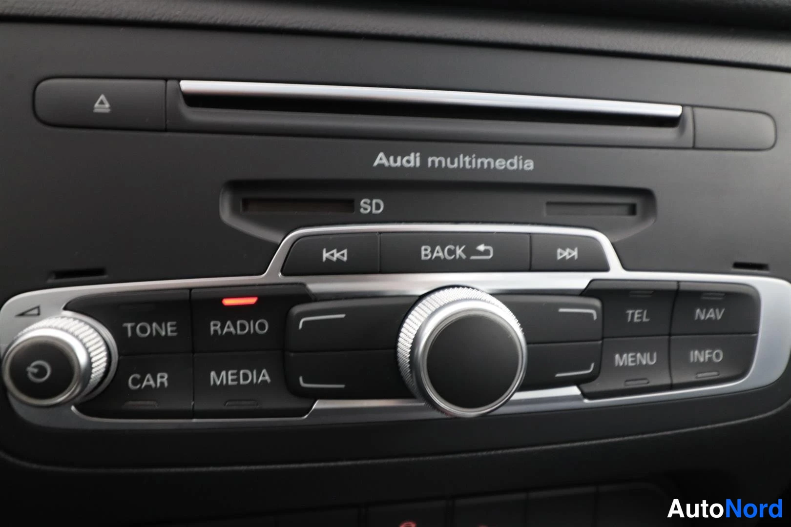 Yksityiskohta: Audi multimedia -yksikkö keskikäytössä: SD-korttipaikka, BACK-painike, säätökiekko ja painikkeet TONE, RADIO, CAR, MEDIA, TEL, NAV, MENU ja INFO.