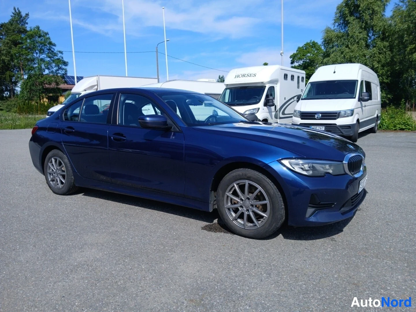 Etuviisto, nokka oikealle: Tummansininen sedan auto kolmesta neljäsosasta edestä oikealta kuvattuna parkkialueella.