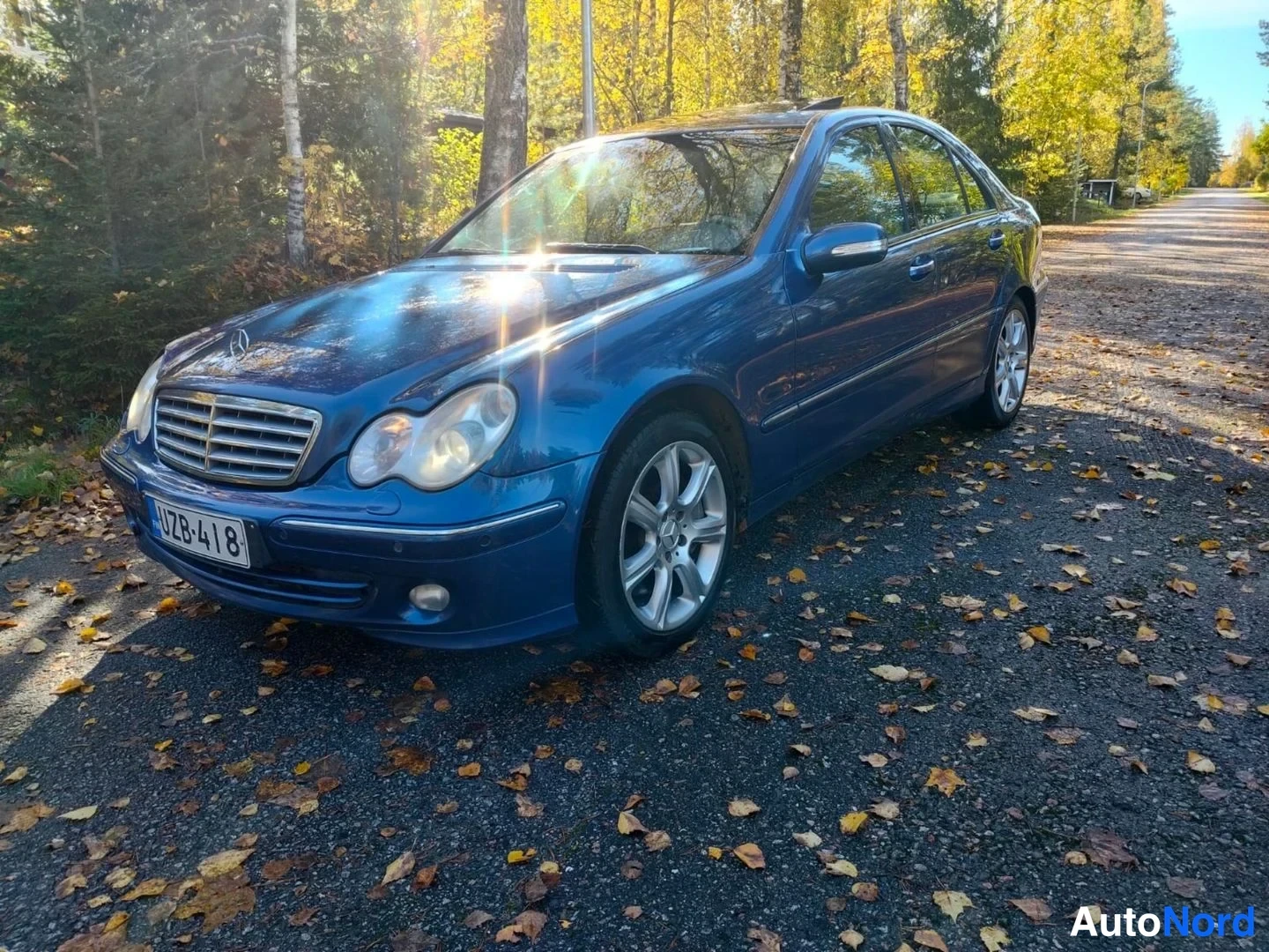 Etuviisto, nokka vasemmalle: Sininen Mercedes-Benz-sedan etunurkasta vasemmalta kuvattuna; etusäleikkö, valot ja kylki näkyvät, rekisteritunnus.