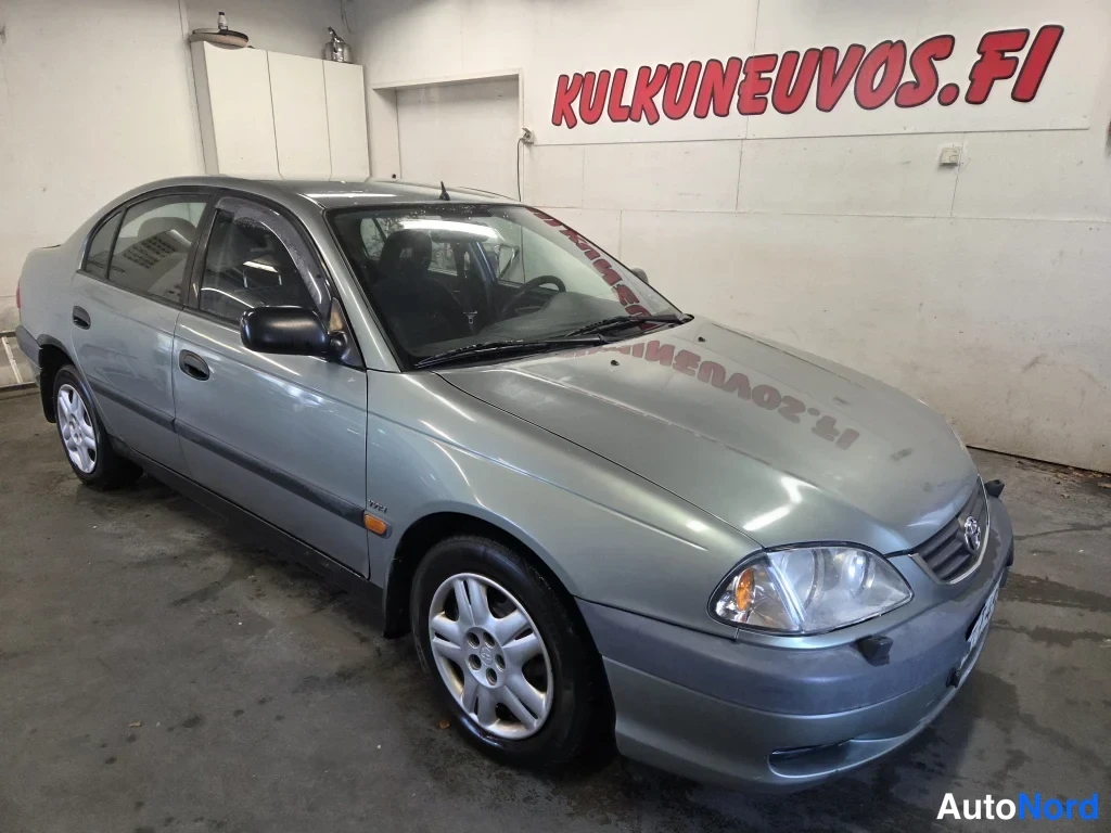 Etuviisto, nokka oikealle: Toyota Avensis -sedanin etukulma vasemmalta, hopeansävyinen korirakenne sisätiloissa.