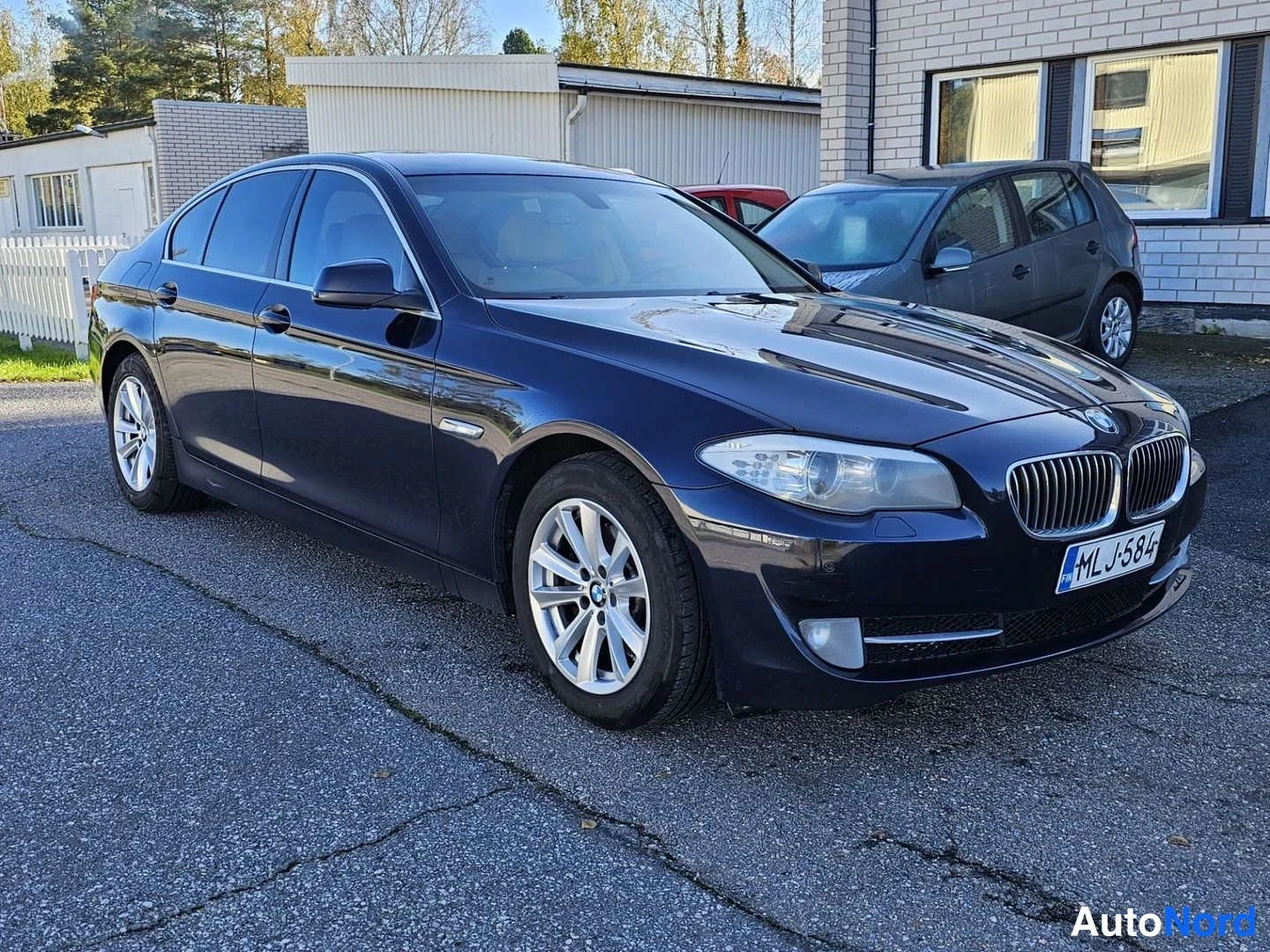 Etuviisto, nokka oikealle: Tummansininen BMW-sedan kolmanneltaa kulmalta edessä oikealle, kaksiosainen etusäleikkö ja rekisterikilpi näkyvissä.