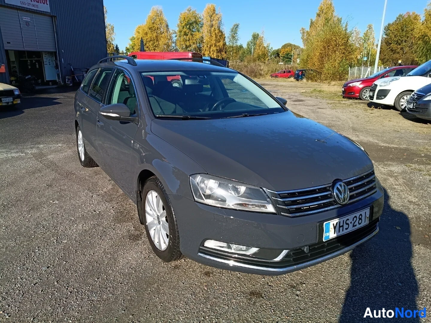Etuviisto, nokka oikealle: Volkswagen Passat -farmari edestä oikealta kolmantenvartta kuvattuna, tummanharmaa kori, rekisterikilpi.