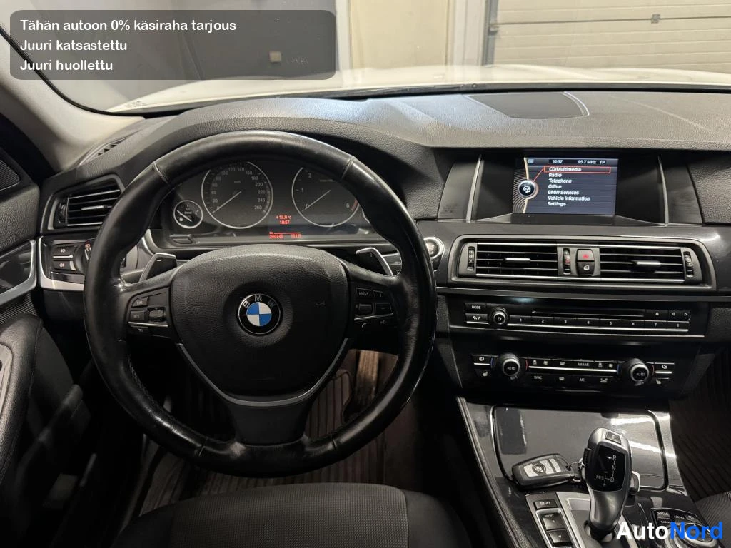Muu: n yleiskuva BMW:n ratin ja kojelaudan kanssa; näkyvissä mittarit, keskikonsolin näyttö ja automaattivaihteen valitsin.