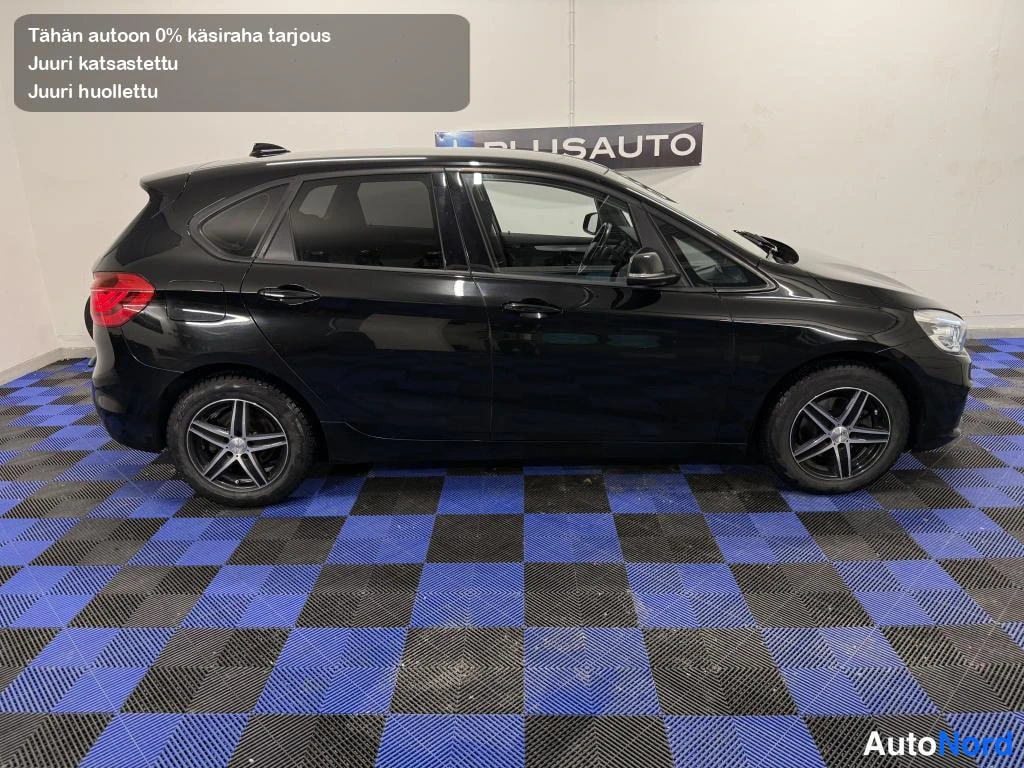 Etuviisto, nokka oikealle: Mustan BMW:n sivukuva sisätiloissa, molemmat pyörät ja ovet näkyvissä sinimustaruutuisella lattialla.
