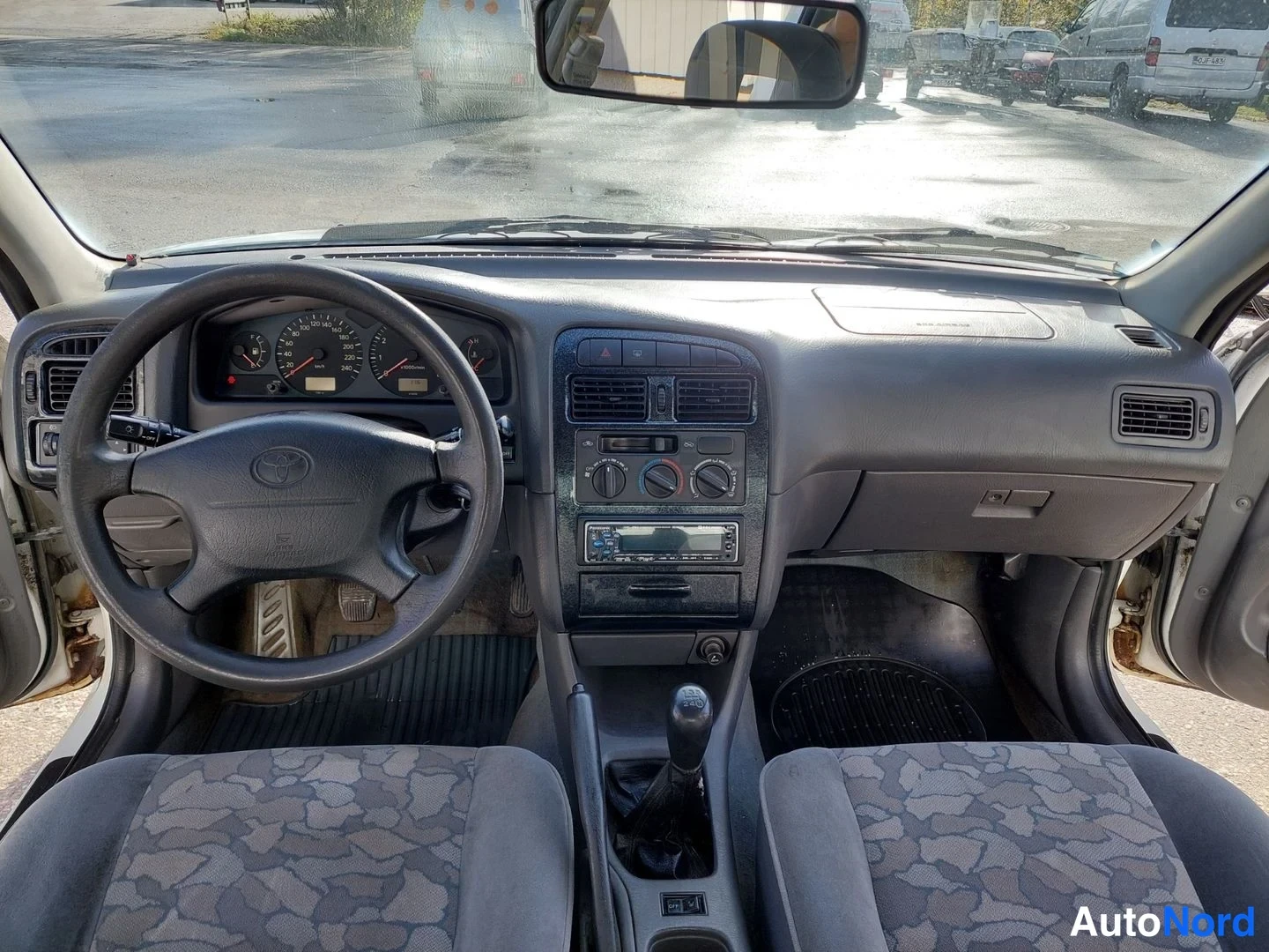 Muu: Kojelauta ylhäältä: Toyota-ohjauspyörä, mittaristo, keskiö konsoli radioineen ja manuaalivaihteiston vaihdekeppi.