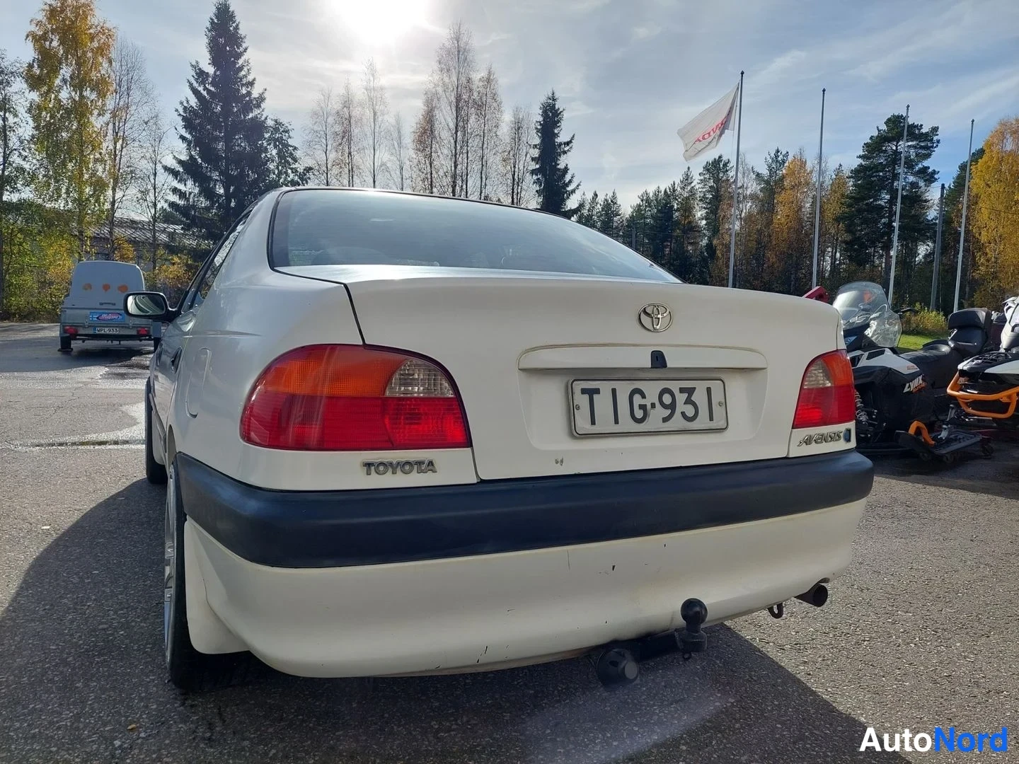 Takaa: Valkoisen Toyota Avensisin perä suoraan takaa: puna-oranssit takavalot, Toyota-merkki, Avensis-teksti ja rekisterikilpi.