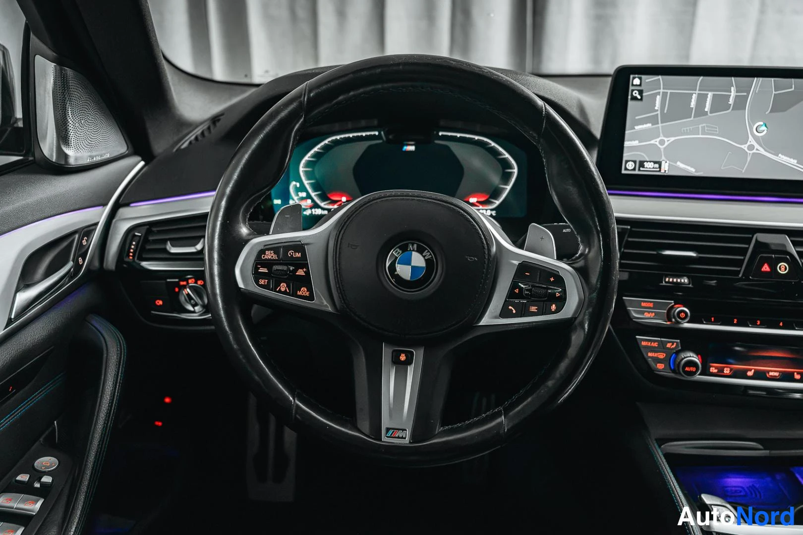 Muu: BMW-ohjauspyörä lähikuvassa: M-merkintä, monitoiminapit, mittaristo ja kartta näyttävä keskushäytta taustalla.