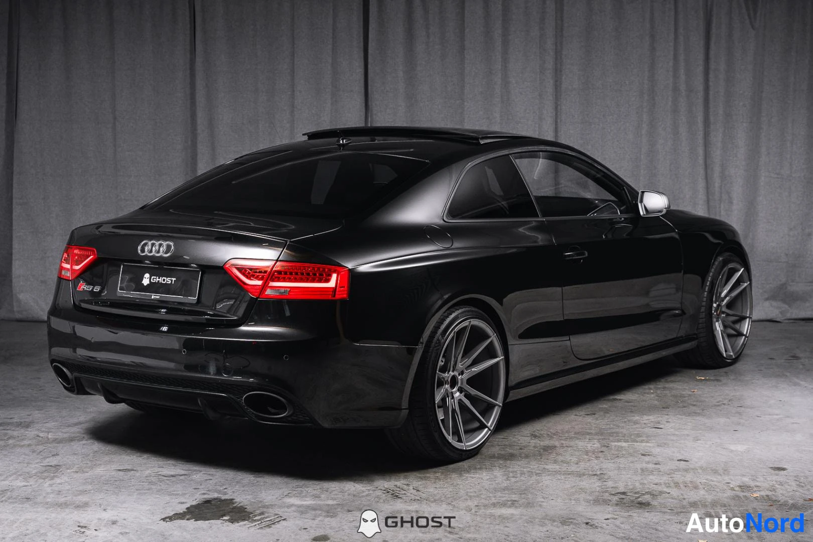 Takaviisto: Mustan Audi RS5 Coupén takakulmakuva: punaiset takavalot, kromilistat ja harmaat kevytmetallivanteet näkyvät studiossä sisätiloissa.
