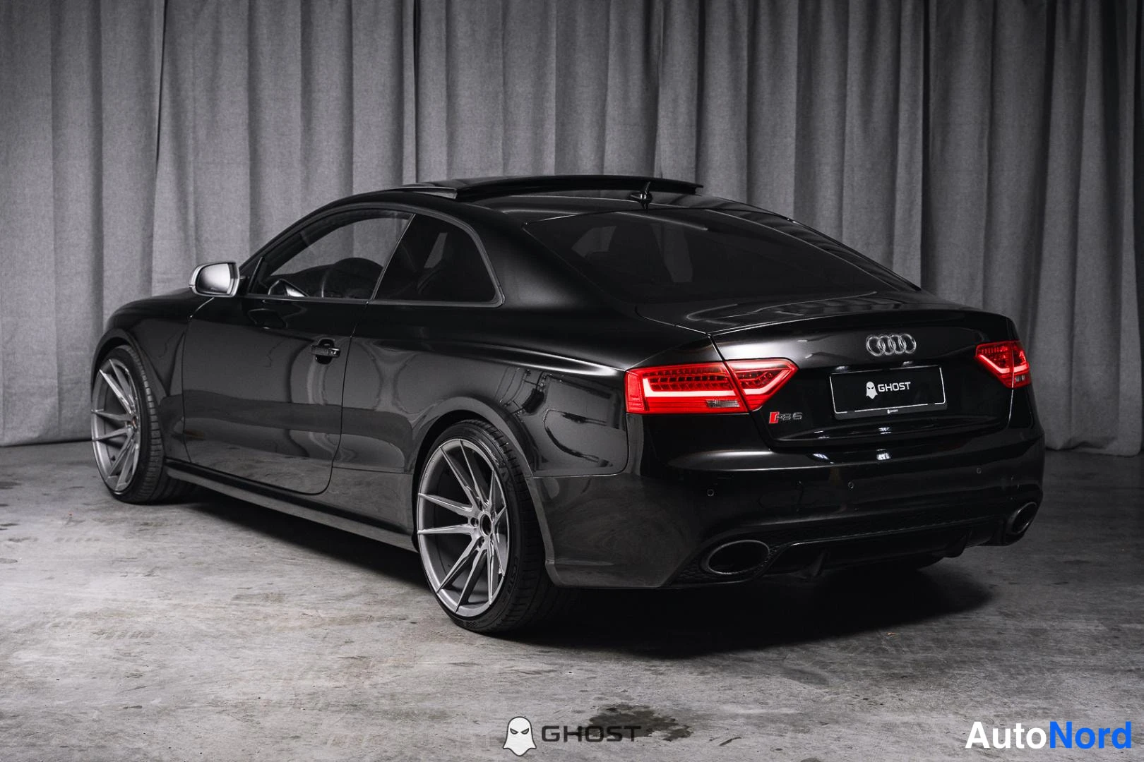 Takaviisto: Mustan Audi RS5 Coupén vasen takakulmakuva: punaiset takavalot, mustat korilevyt ja harmaat kevytmetallivanteet.