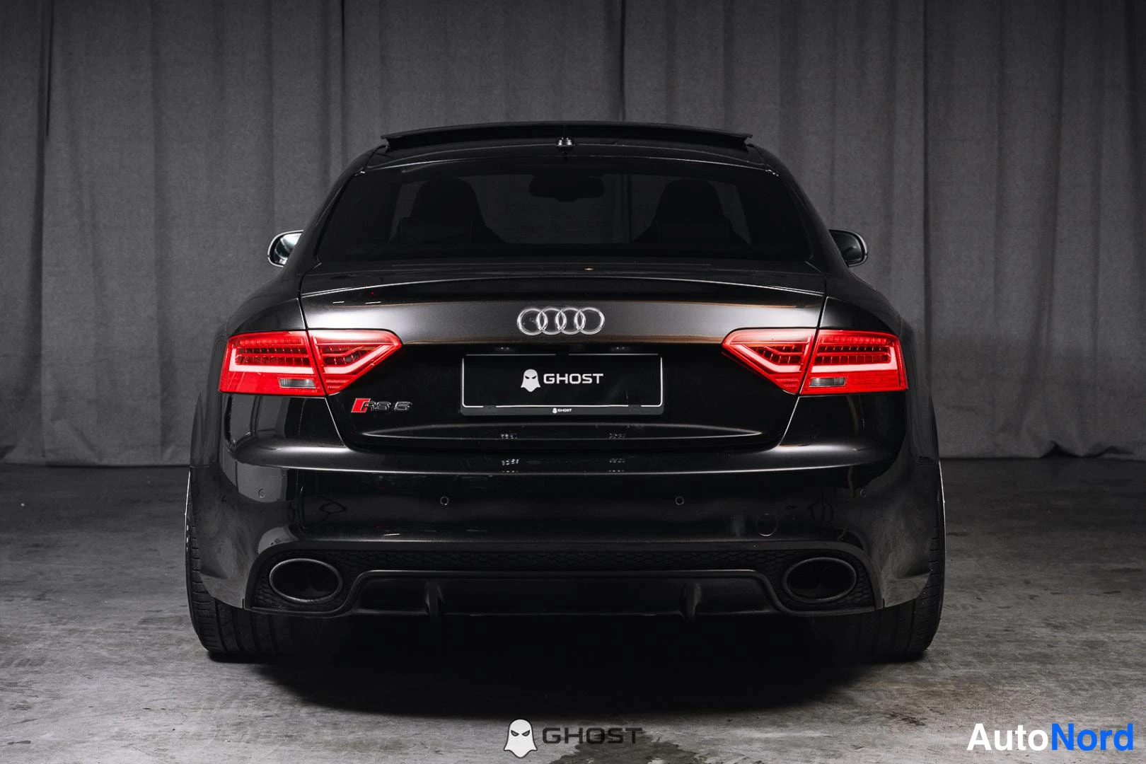 Takaa: Mustan Audi RS5 Coupén suora takanäkymä: punaiset takavalot, mustan sävyinen lasi ja kaksi pakoputkea näkyvät takapuskurissa.