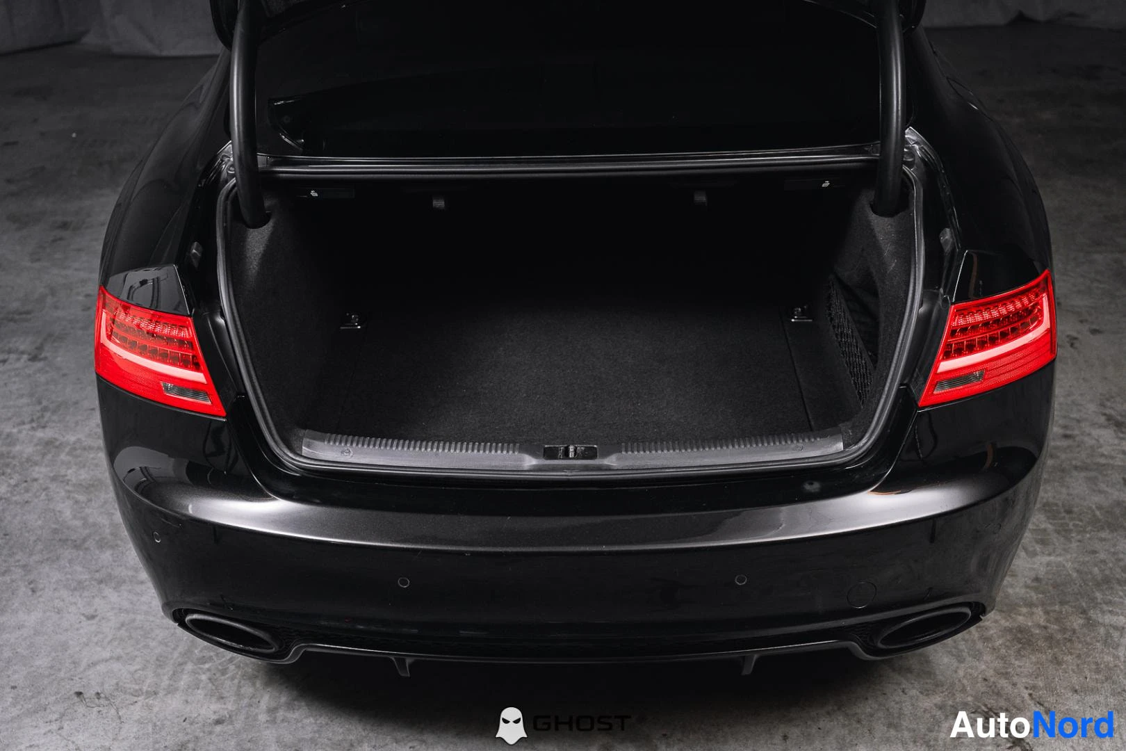 Takaa: Mustan Audi RS5 Coupén avattu tavaratila kuvattuna ylhäältä takaosaan: tumma ahtoontokaistale ja kaksi pakoputkea näkyvät takaossan alla.