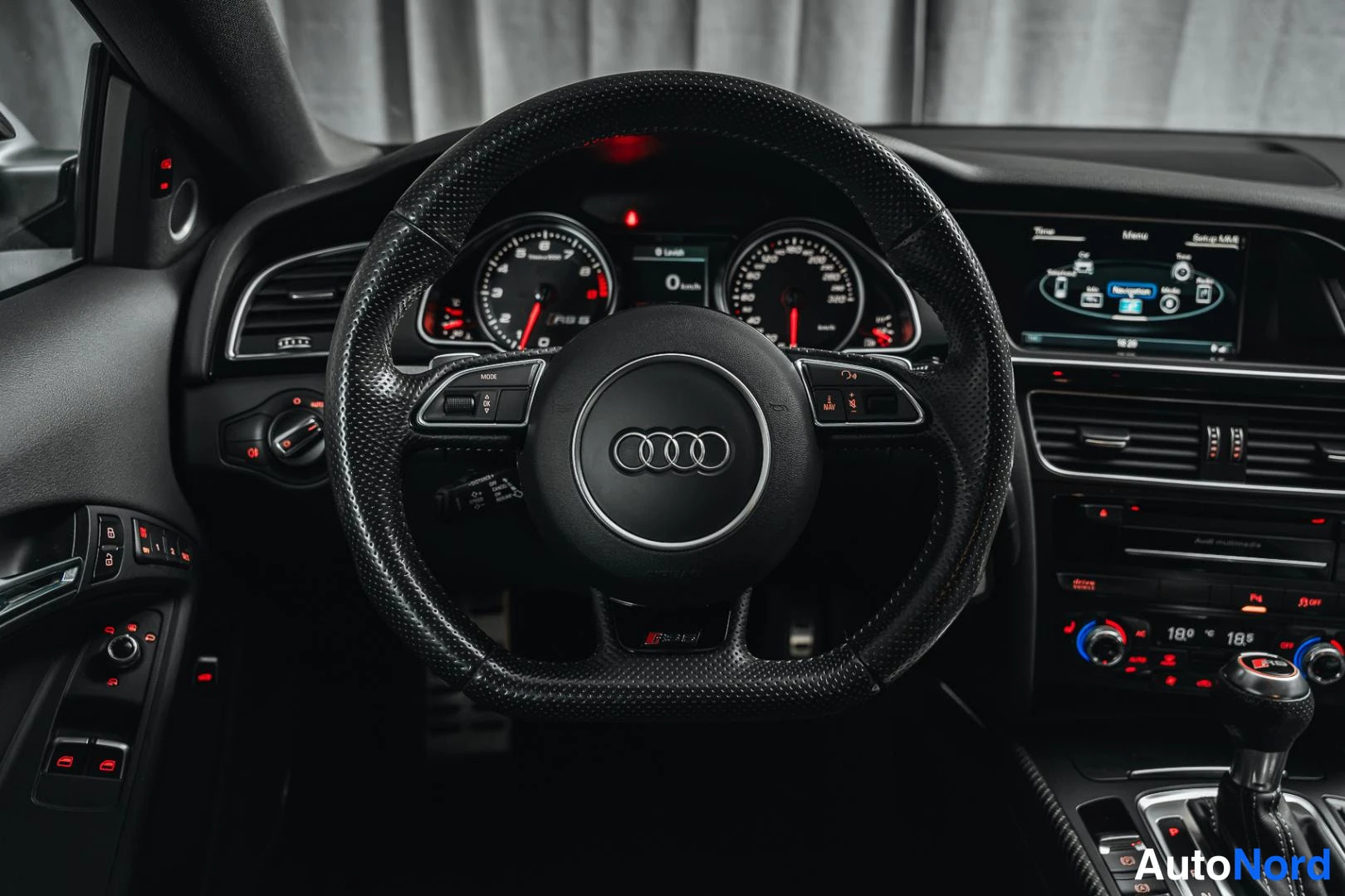 Muu: Ohjauspyörä ja kojelauta lähikuvassa: Audi-merkki ohjauspyörässä, mittarit ja keskusnäyttö.