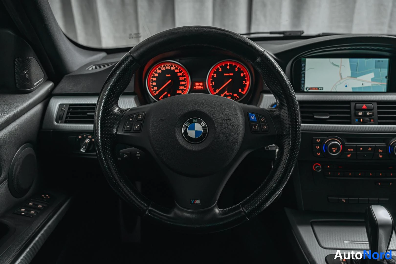 Muu: Lähikuva ohjauspyörästä ja kojelaudasta: BMW-ohjauspyörä, punaiset valaistut mittarit ja kartta näytöllä.