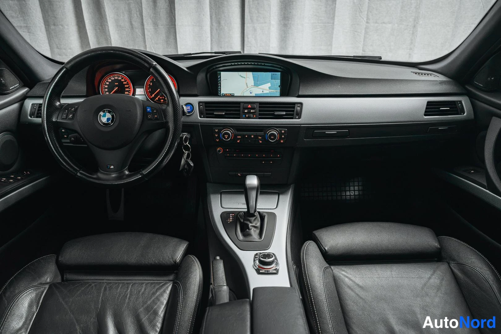Muu: Auton sisätilat etualalta: BMW-ohjauspyörä, punataustaiset mittarit, keskikonsolissanavigation näyttö ja automaattivaihteiston valitsin.