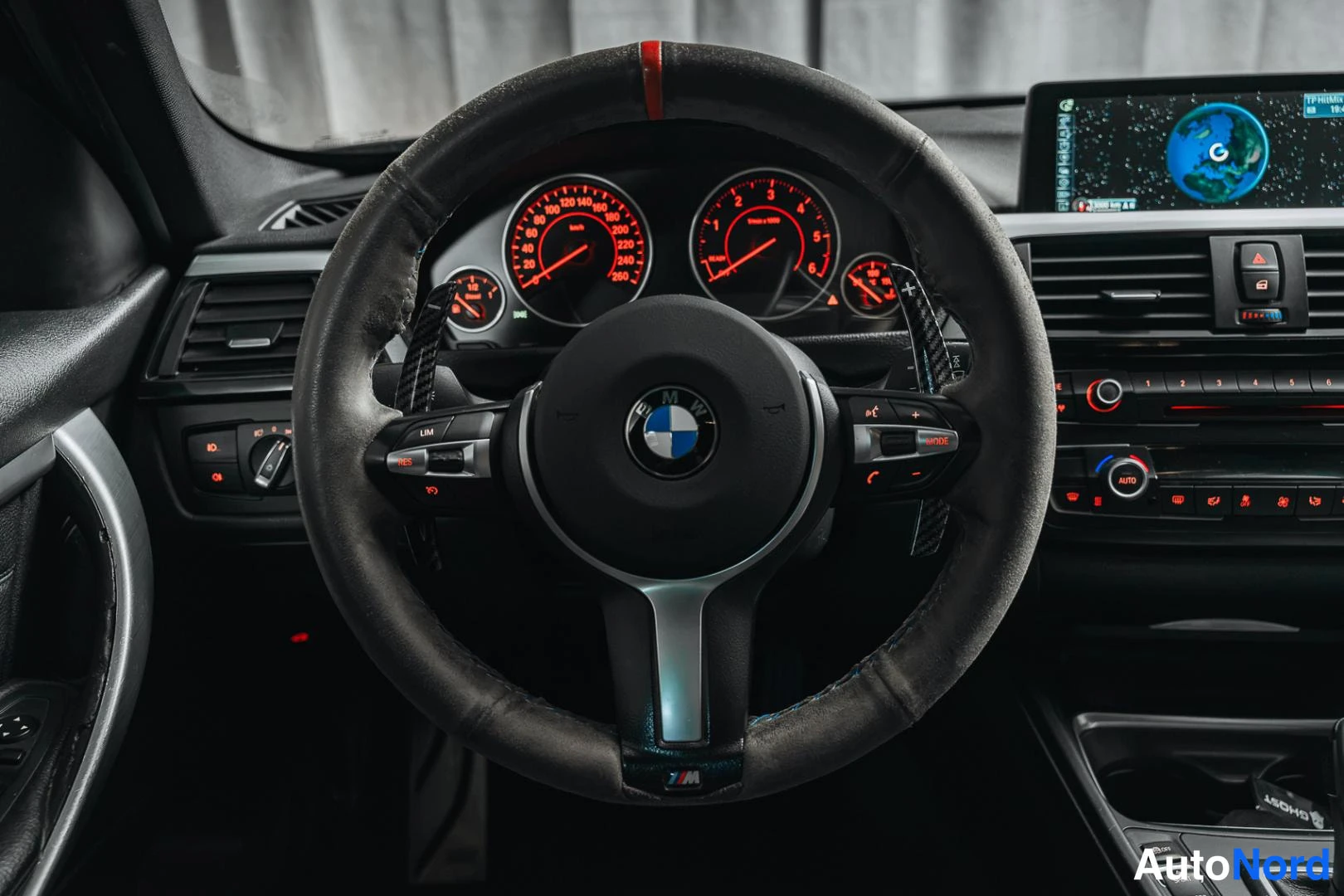 Muu: Lähikuva BMW-ohjauspyörästä ja punaisella valaistusta mittaristosta; karkeaverhoillun ohjauspyörän takana hiilikuituiset vaihteenannospadat.