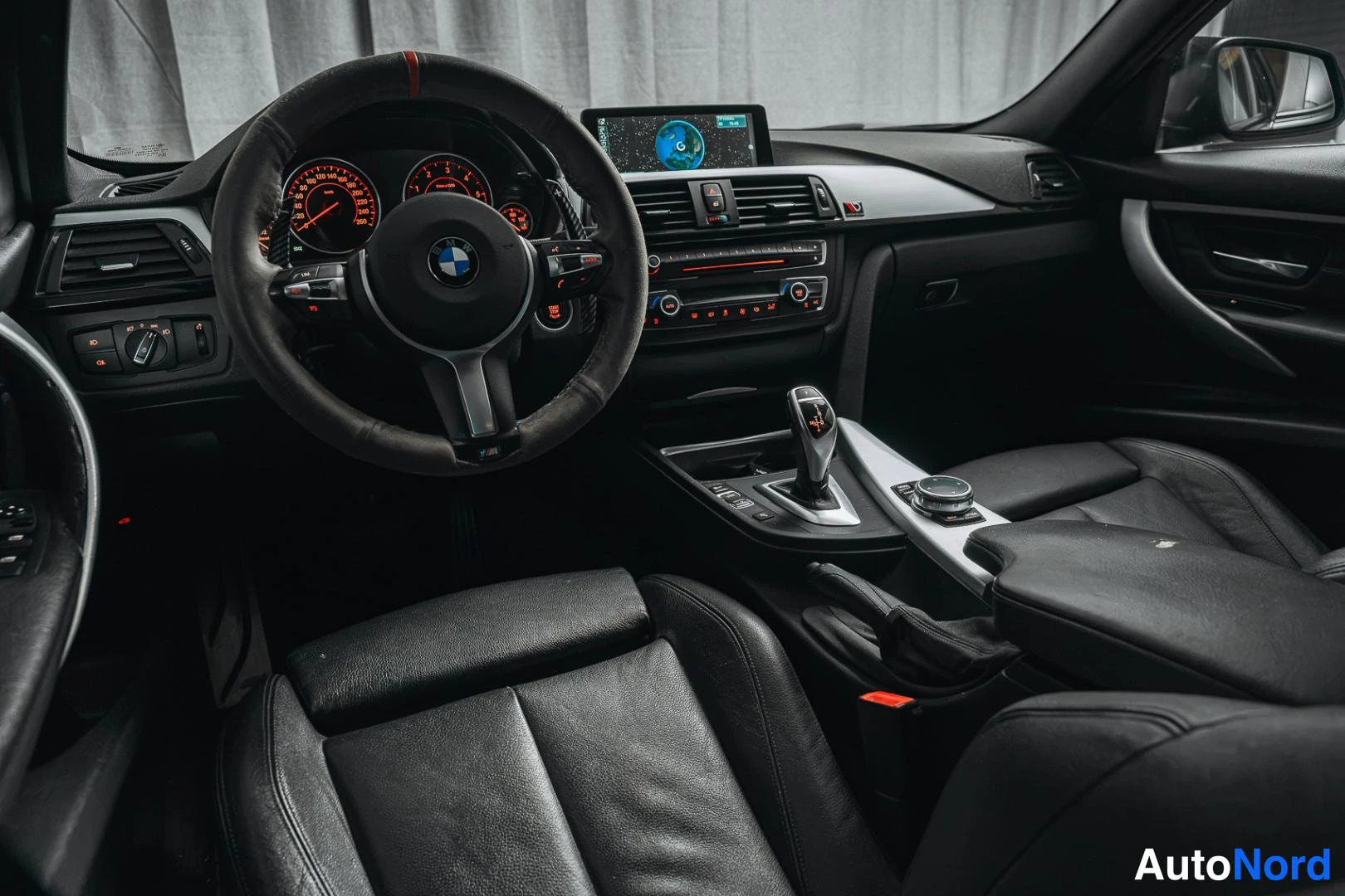 Muu: Kuljettajan puolen näkymä sisätilaan: BMW-ohjauspyörä, analogiset mittarit, keskikonsolin automaattivalitsin, iDrive-ohjain ja näytöllä oleva kartta.