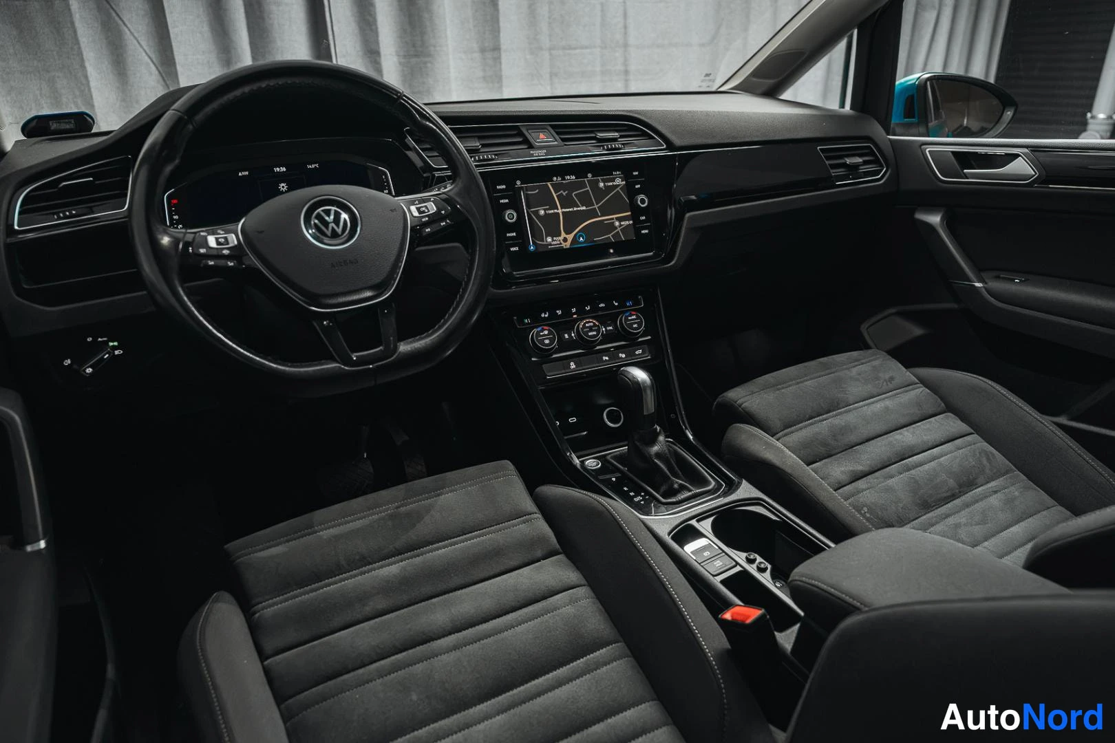 Muu: Ohjaamo matkustajan puolelta katsottuna: Volkswagen-ohjauspyörä, digitaalinen mittaristo, navigointinäyttö, automaattivaihteisto ja tummat penkkiistuimet.
