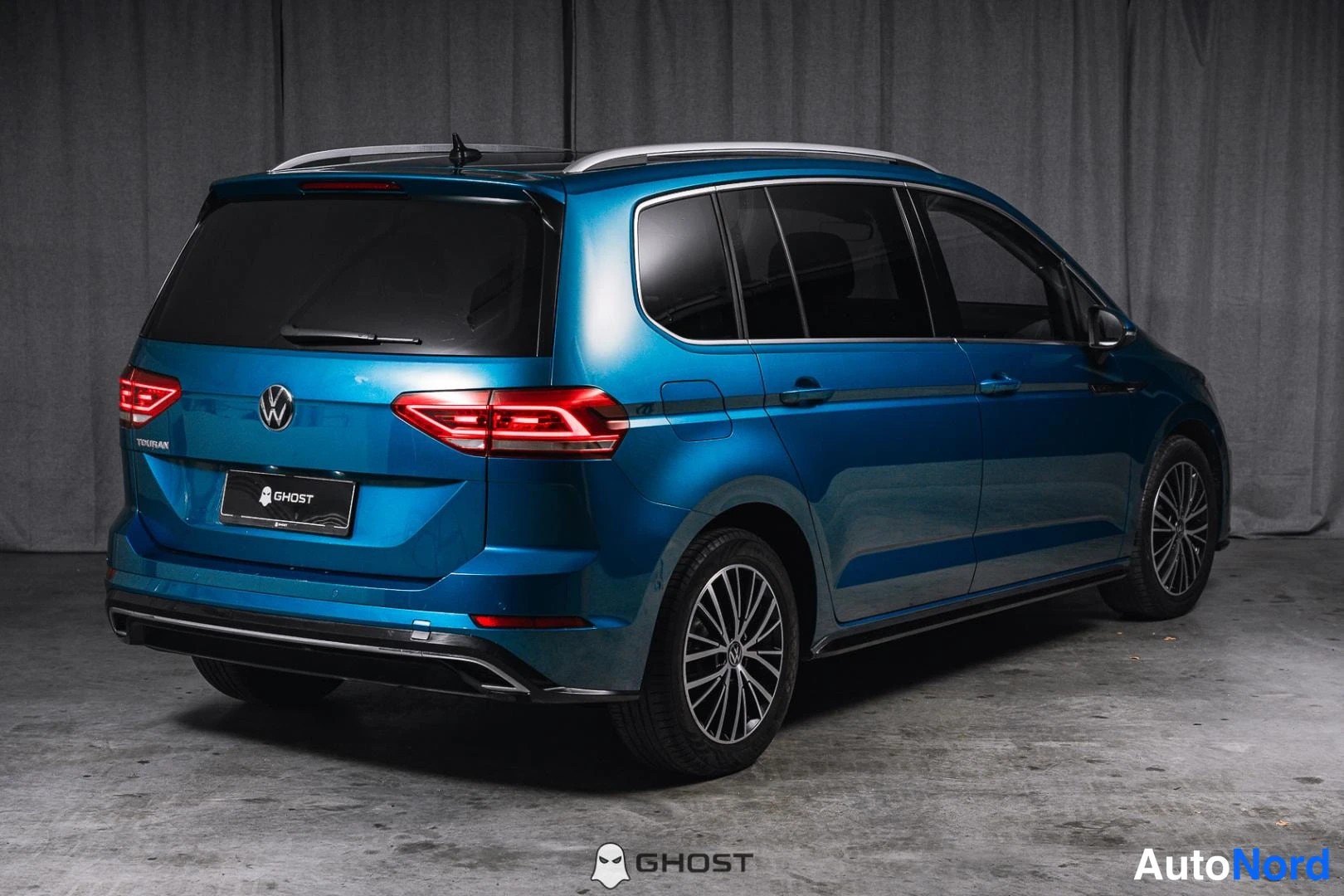 Takaviisto: Sininen Volkswagen Touran takaapäin vasemmasta kolmasosakulmasta, takaosa ja kylki näkyvissä.