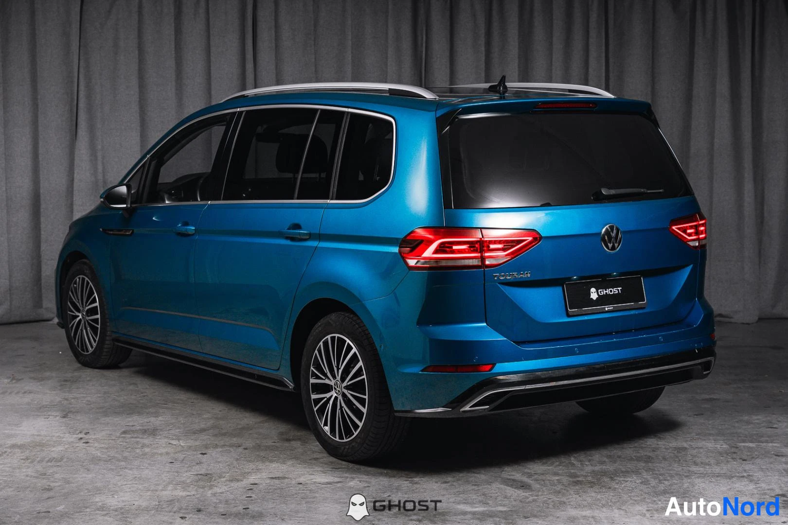 Takaviisto: Sininen Volkswagen Touran takaapäin oikeasta kolmasosakulmasta, takaosa ja kylki näkyvissä.