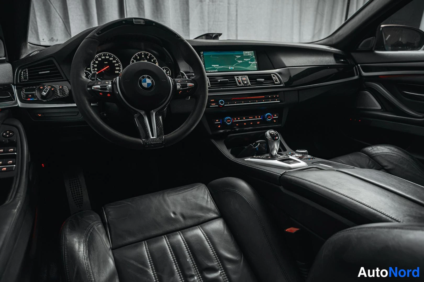 Muu: Ohjaamo kuljettajan puolelta: BMW-ohjauspyörä, mittaristo, karttanäytöllä varustettu keskikonsoli ja mustat nahkaistuimet.