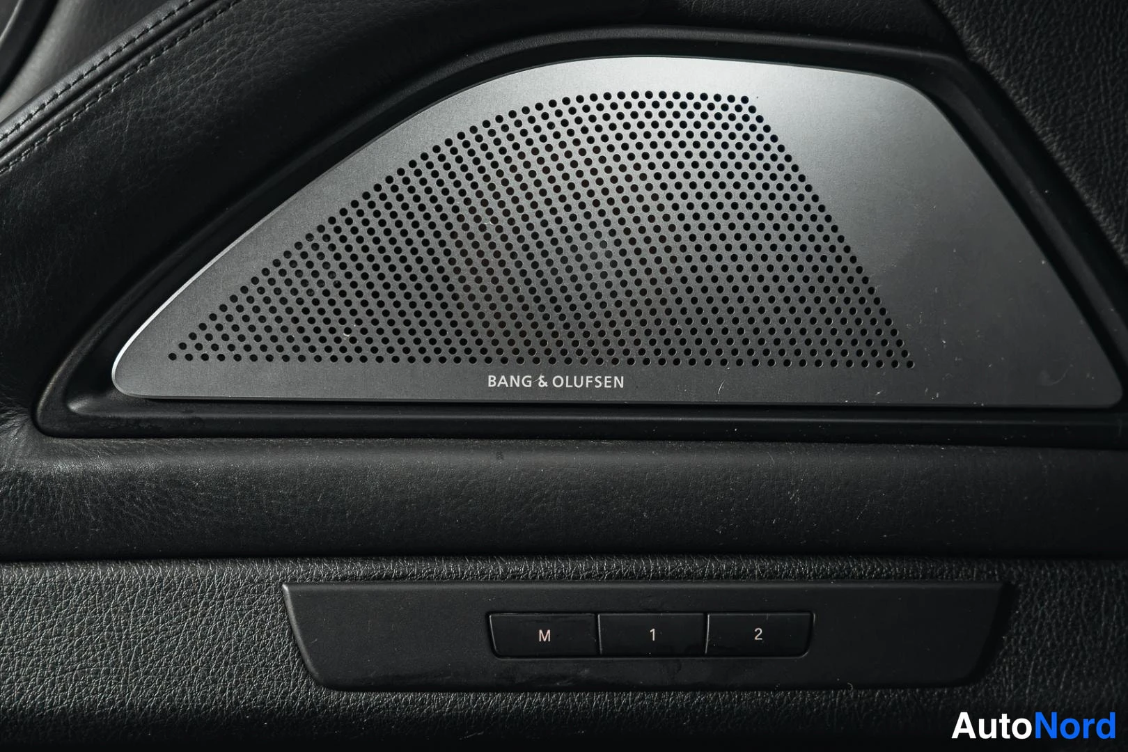 Muu: Bang & Olufsen -kaiuttimen hifiverhoilu ovessa, alapuolella M-, 1- ja 2-painikkeet.