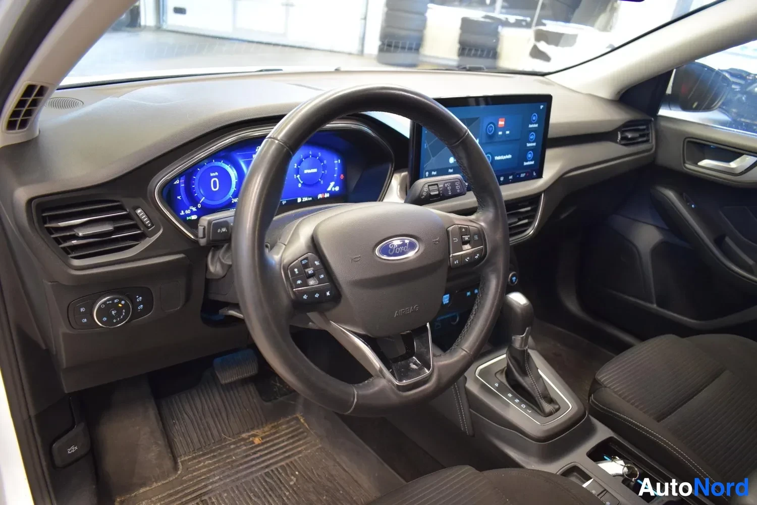 Muu: Ohjaamo kuvattuna kuljettajan oven suunnasta: Ford-ohjauspyörä, digitaalinen mittaristo, keskellä iso kosketusnäyttö ja automaattivaihteiston valitsin, tummat k