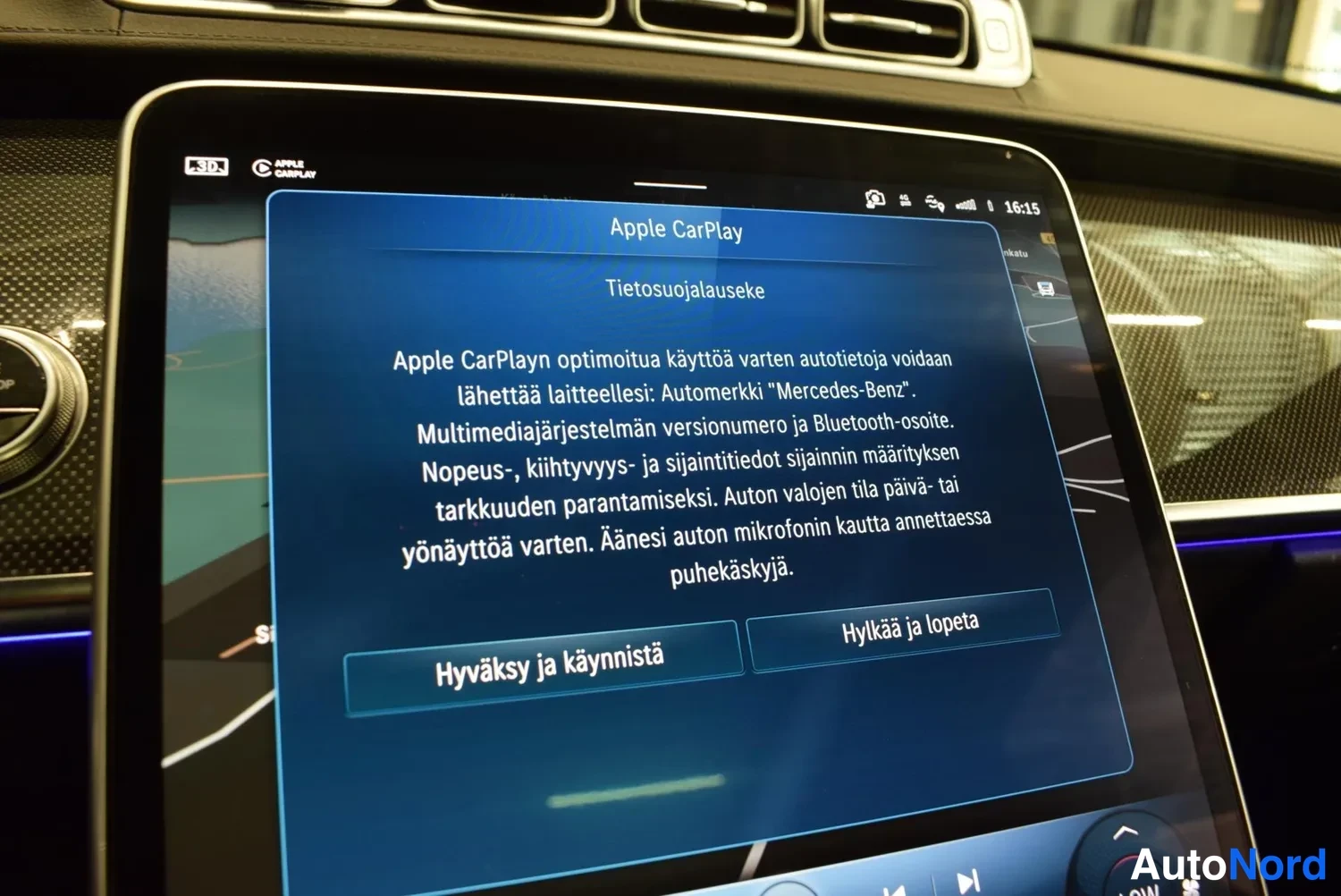 Yksityiskohta: Keskikonsolin näytön lähikuva: näytöllä on 'Apple CarPlay' -käyttöliittymä, jossa on suomenkielinen tietosuojailmoitus ja painikkeet 'Hyväksy ja käynnistä' sekä