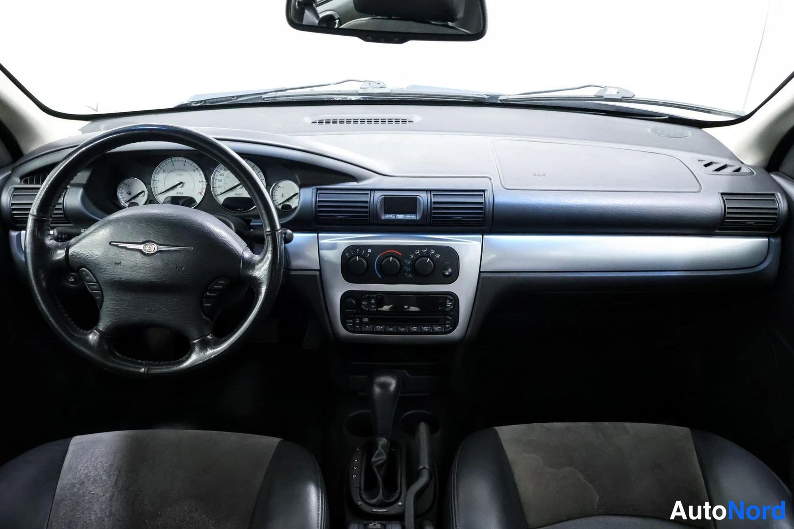 Yksityiskohta: Ohjaamo vasemmalta kuvattuna: tumma kojelauta, Chrysler-merkitty ohjauspyörä, instrumentit, manuaalikäyttöinen ilmastointipaneeli, radio ja automaattivaihteen v