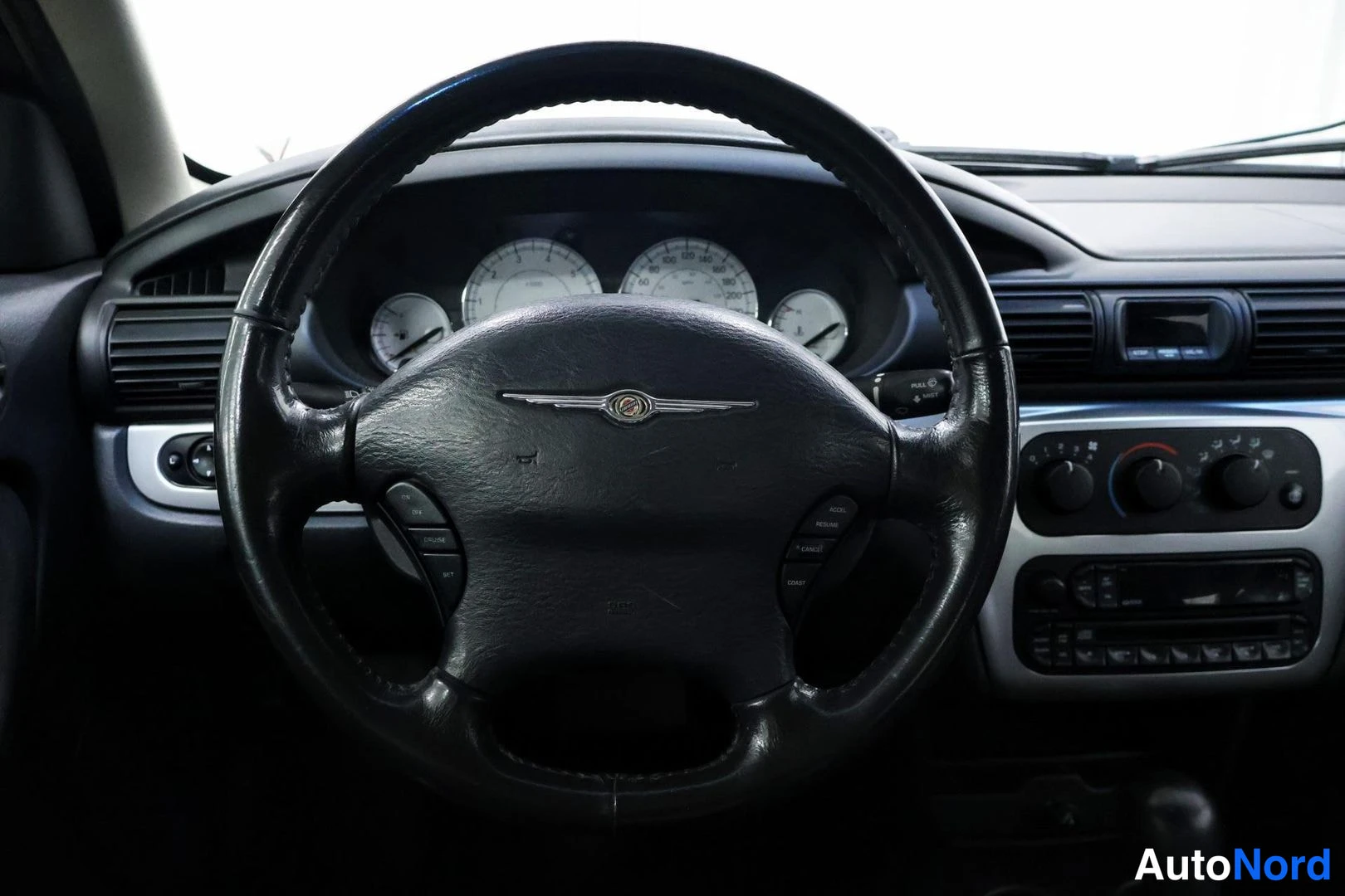 Yksityiskohta: Lähikuva Chrysler-ohjauspyörästä; puhelin- ja äänitoiminnot sekä muut painikkeet pinnillä, mittaristo taustalla.