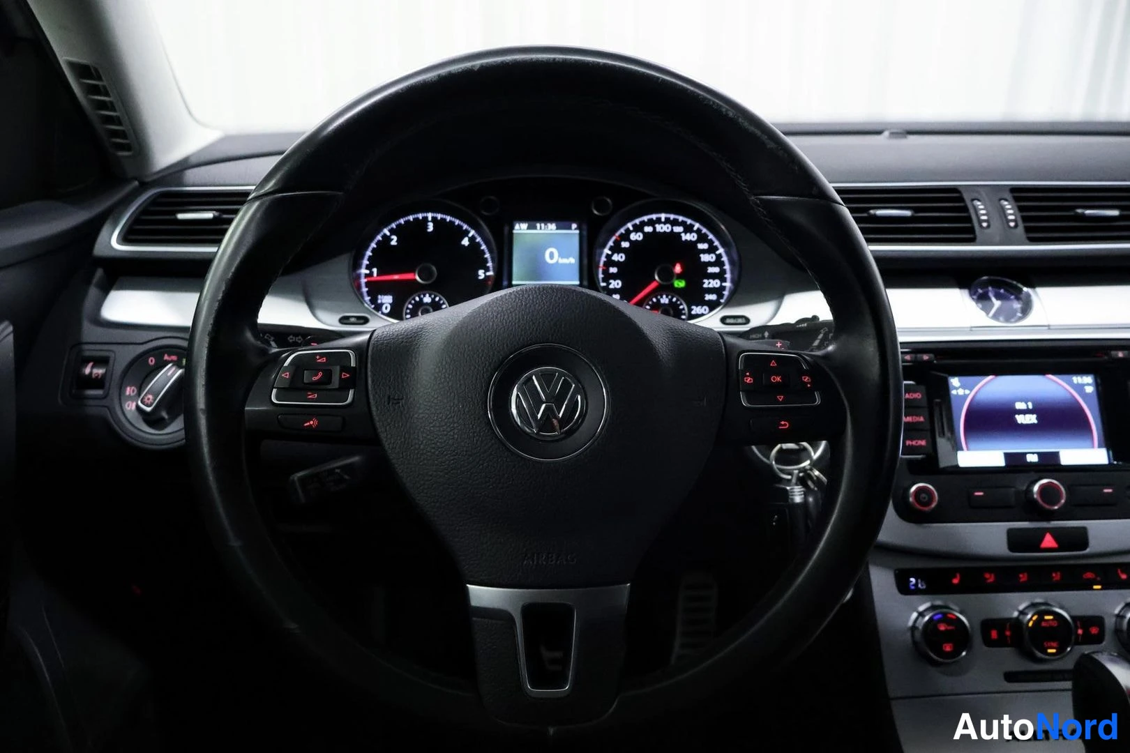 Muu: Volkswagen-ohjauspyörän lähikuva, taustalla mittaristo näytöllä '0 km/h' ja radiopaneeli.