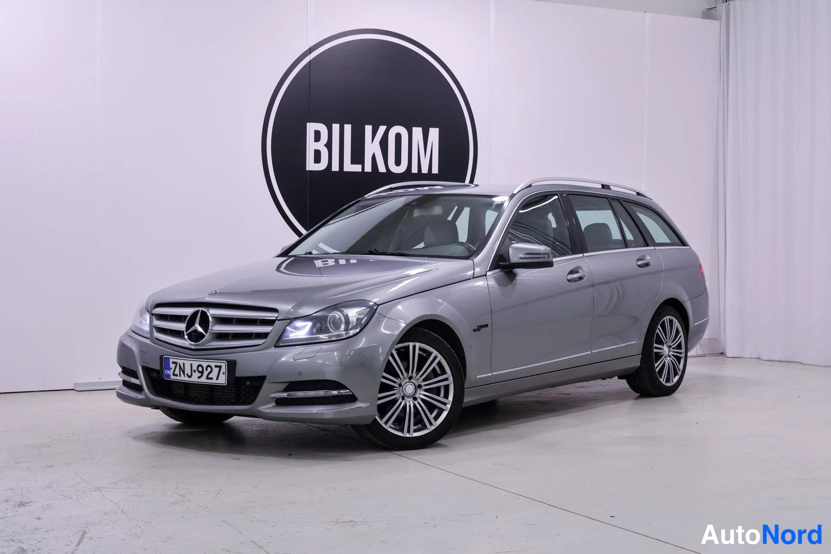 Etuviisto, nokka vasemmalle: Mercedes-Benz C -farmari kolmivärikuvassa edestä vasemmalta, hopeanharmaa, rekisteritunnus.