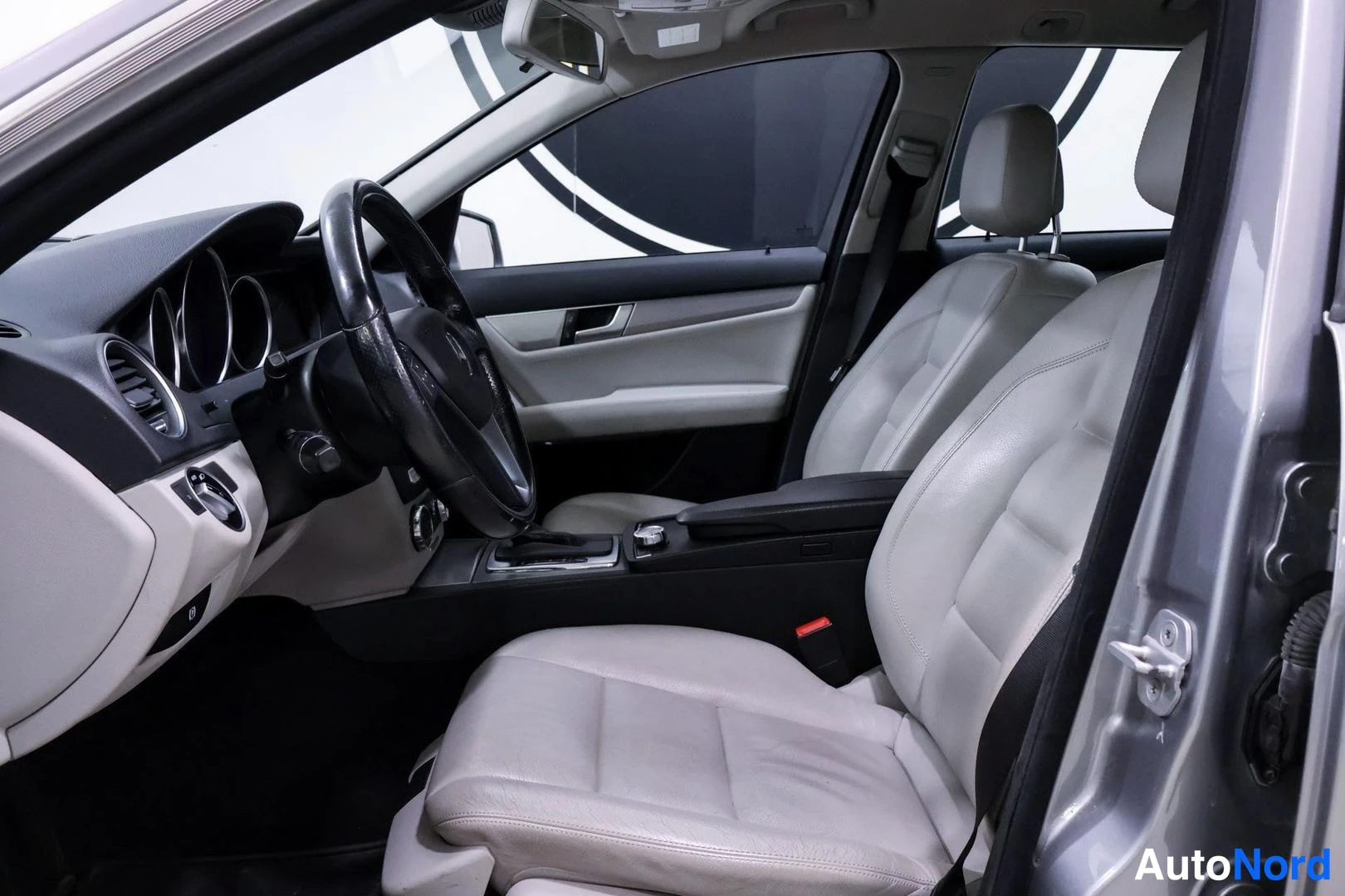 Muu: Mercedes-Benzin sisätilat: vaalea nahkapenkit, ohjauspyörä ja kojelauta kuvattuna etumatkalta ovelta katsottuna.