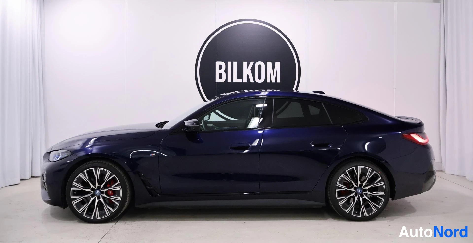 Takaviisto: Sininen BMW i4 sivuprofiilista oikealta kuvattuna sisätiloissa.