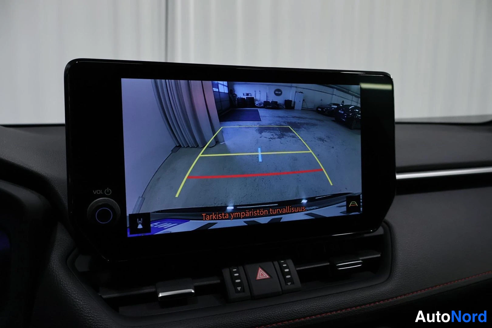 Yksityiskohta: Close-up of the dashboard center console featuring a touchscreen infotainment system displaying a reverse camera feed with yellow and red dynamic guidance lines
