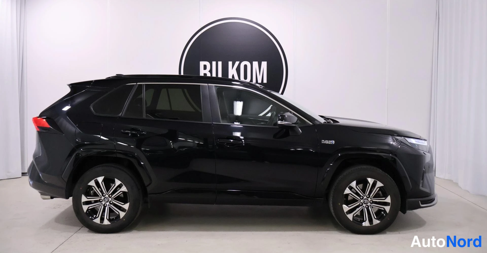Sivulta: Musta Toyota RAV4 -tyyppinen katumaasturi näkyy täydestä profiilista. Autossa on kaksiväriset alumiinivanteet ja 'HYBRID'-tunnus etusivalla. Valot ja perä ovat