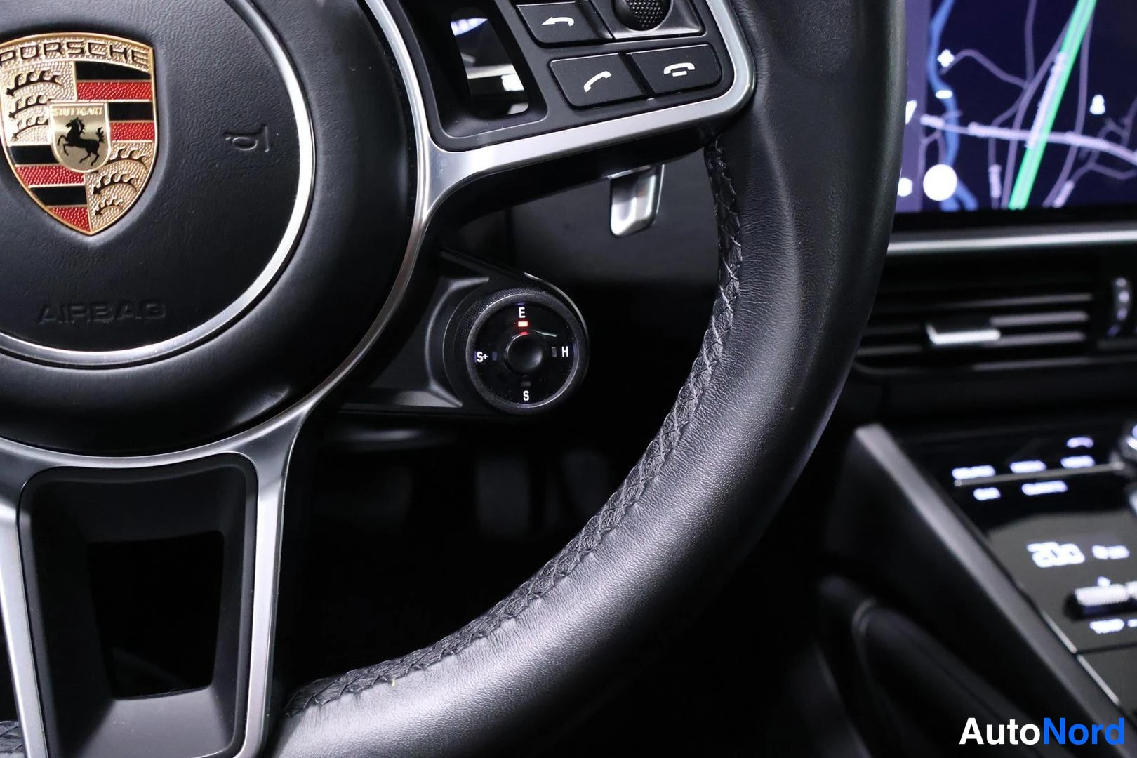 Yksityiskohta: Close-up view of the leather steering wheel with multifunction buttons and paddles. The Porsche crest is visible on the hub.