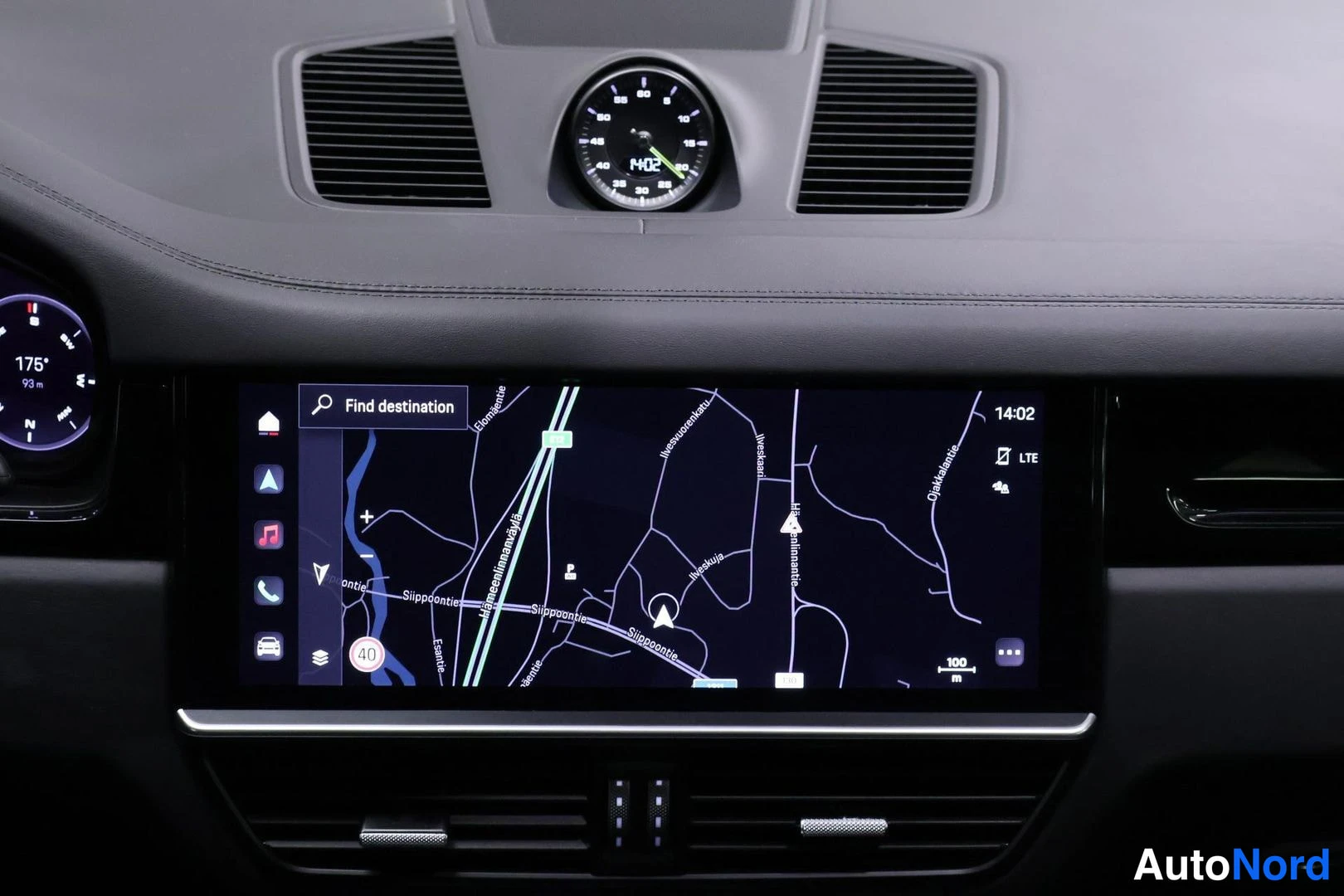 Ohjaamo: Dashboard view featuring a central clock flanked by air vents and a widescreen navigation map displaying 'Find destination'. A digital gauge is partially visibl