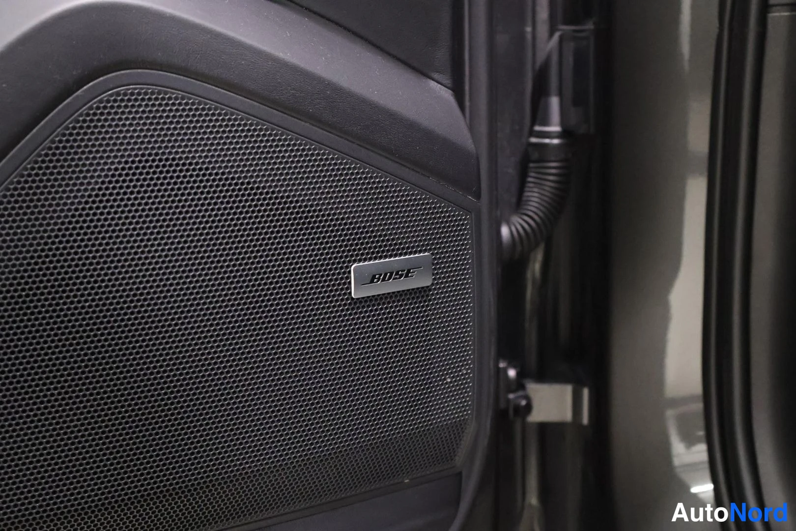Yksityiskohta: Close-up of a speaker grille on an interior door panel showing a metallic badge with the text 'BOSE'.