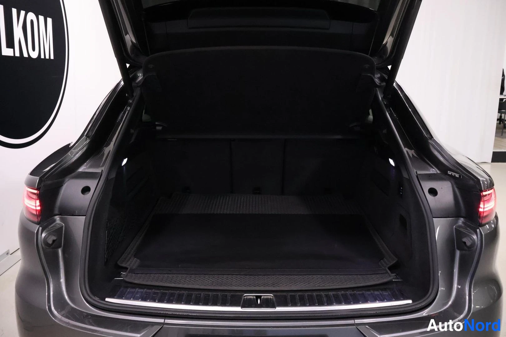 Tavaratila: Rear shot of a dark grey vehicle with the tailgate fully open, revealing a black cargo mat and side lights. The car's exterior paint color is clearly visible on