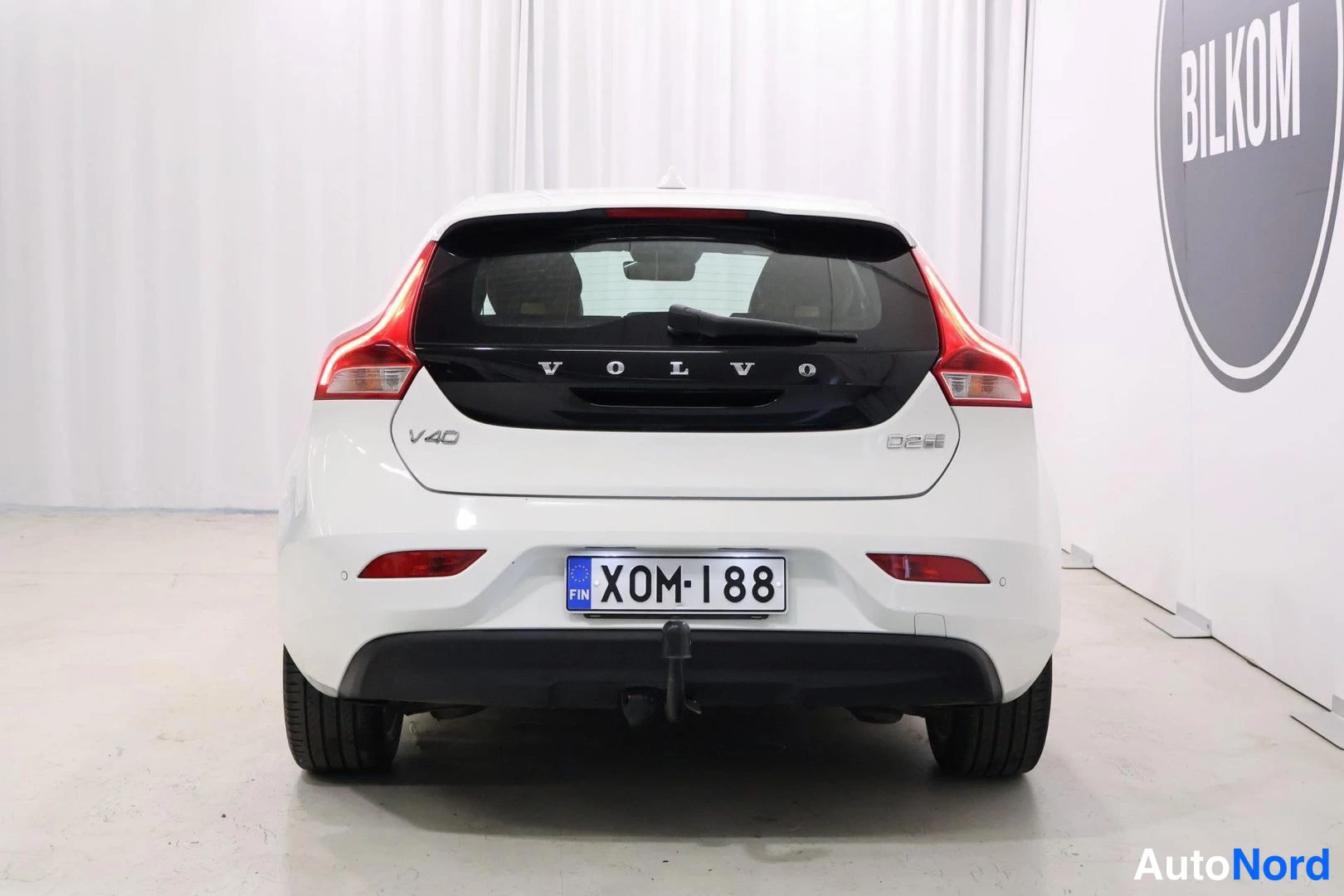 Takaa: Valkoisen farmariauton takaosan suoranäkymä; VOLVO- ja V40-tekstit takaluukussa, rekisterikilpi ja D2-merkintä.