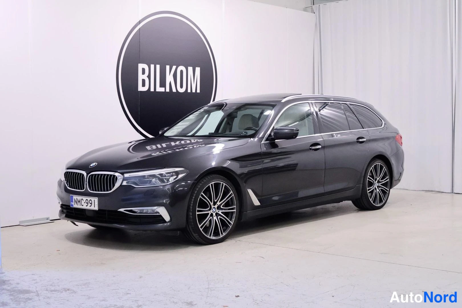 Etuviisto, nokka vasemmalle: BMW 5-sarjan farmariauto tummanharmaassa värissä kolmanneltä osakulmalta, keula vasemmalla.
