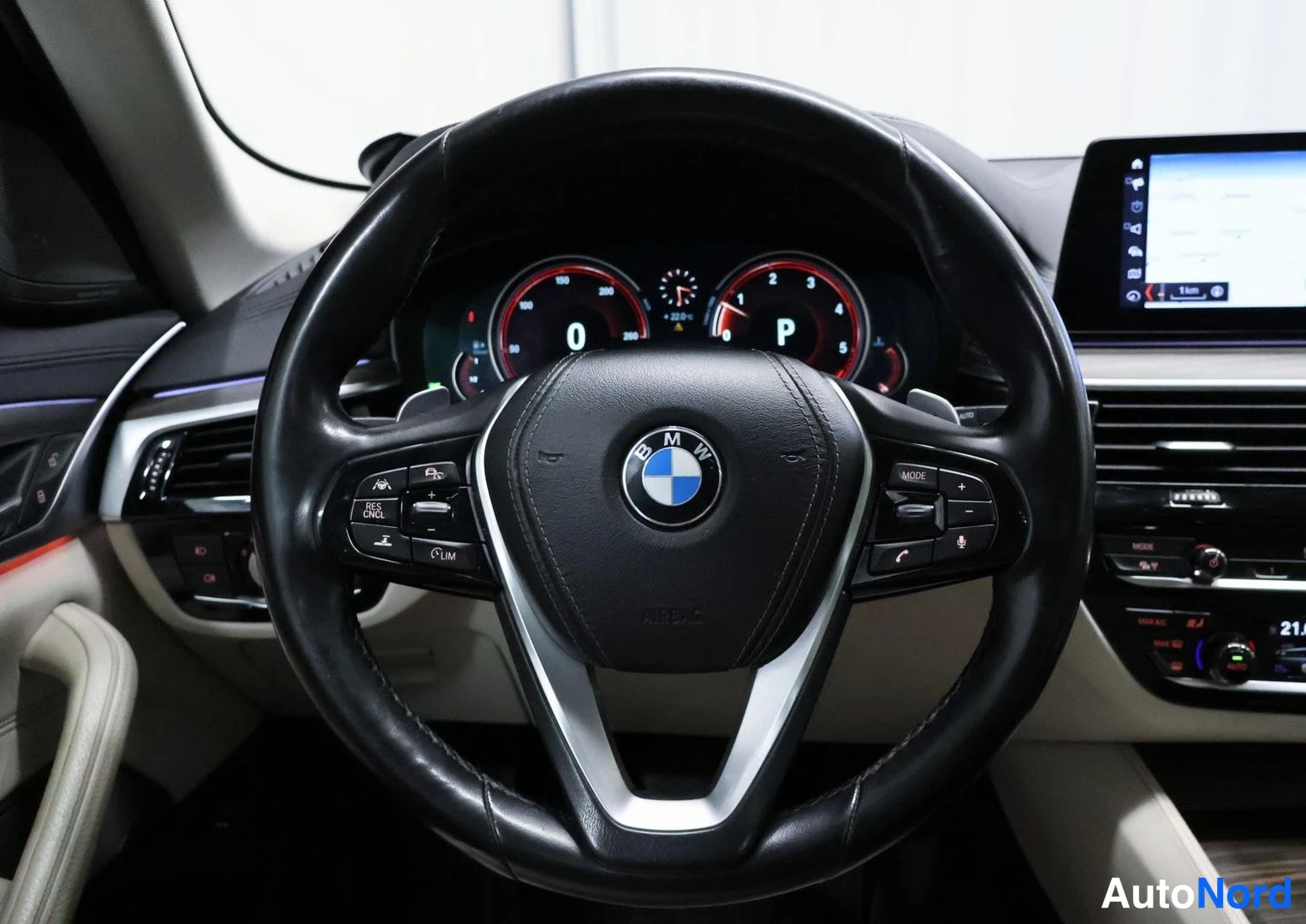 Etuviisto, nokka oikealle: Ohjauspyörä BMW-tunnuksella, digitaalinen mittaristo ja infotainment-näyttö istuimelta kuvattuna.