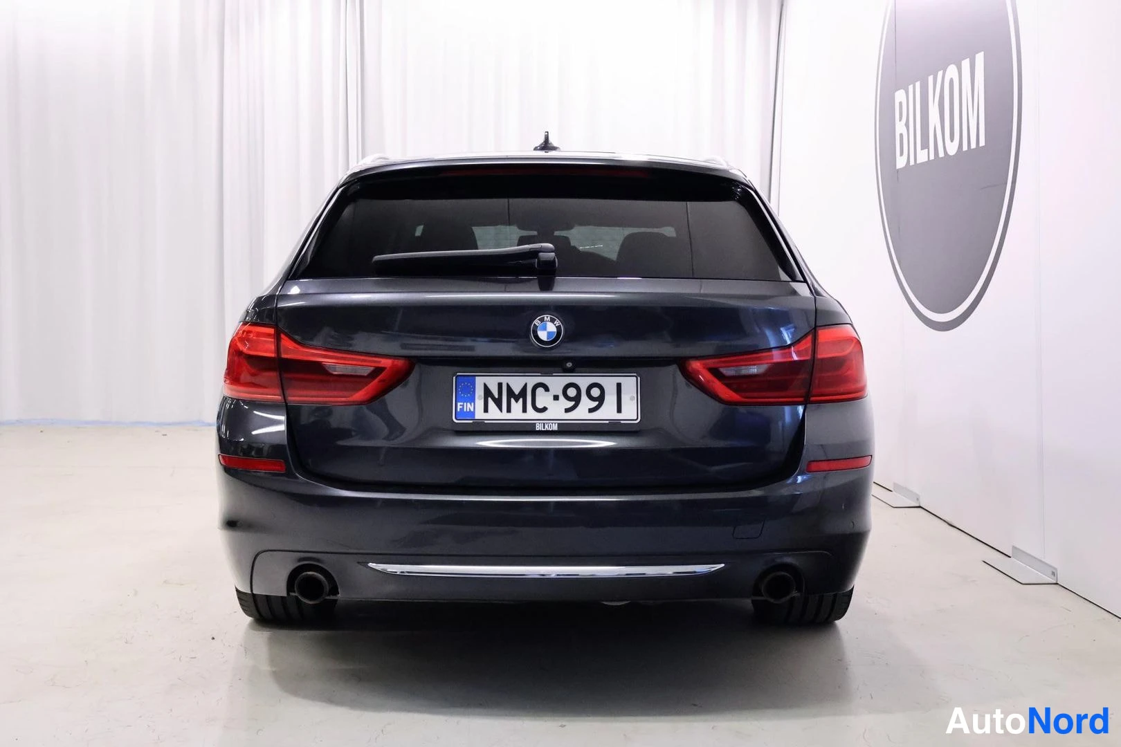 Takaa: Tummanharmaan BMW Touring -farmarin suora takakuva, punaiset takavalot, -rekisterikilpi ja kaksoispakoputket.