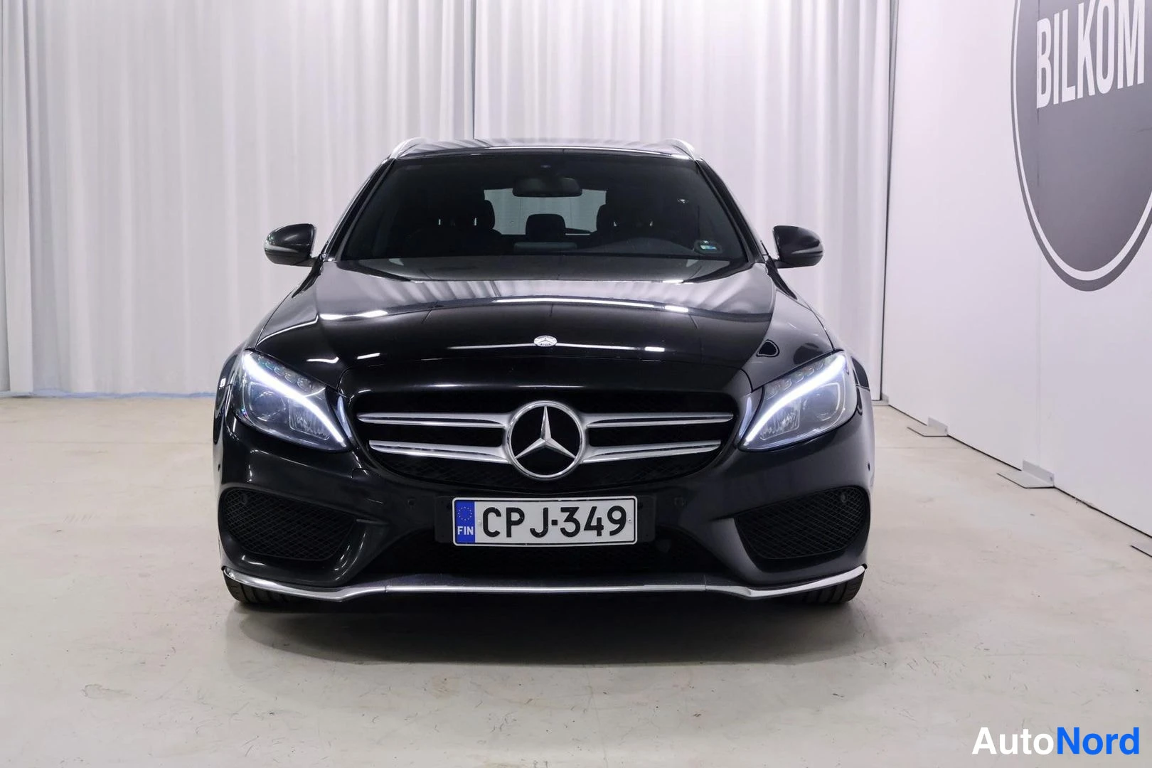 Edestä: Musta farmariauto edestä: etusäleikkö Mercedes-tähdellä, sumut ansaan valot päällä ja rekisteri.