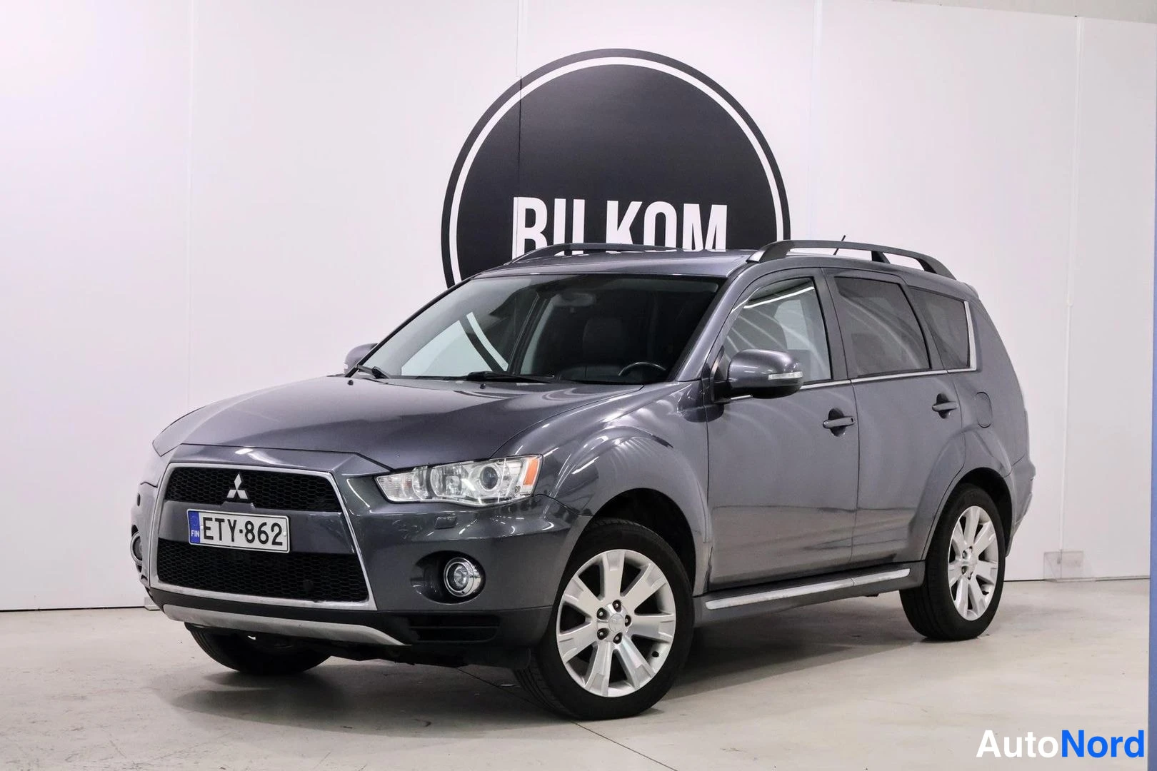 Etuviisto, nokka vasemmalle: Kaksi etukulmaa. Harmaan Mitsubishi Outlanderin etuosa ja oikea kylki näkyvät. Autossa on alumiini-kevytmetallivanteet.
