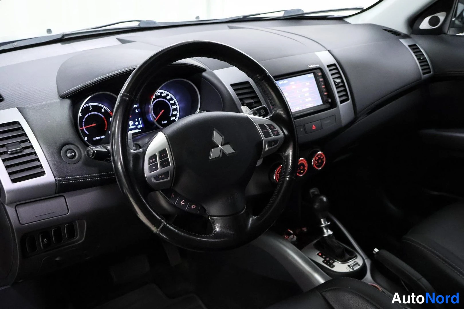 Muu: Mitsubishi steering wheel with multifunction buttons, illuminated instrument cluster, central infotainment screen, red climate control knobs, and automatic gear
